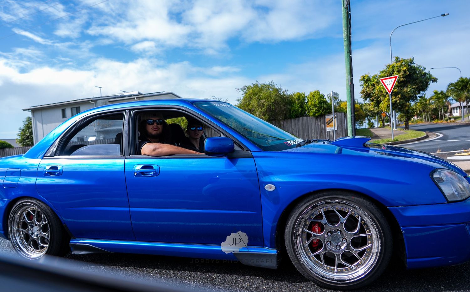 A bright blue Subaru WRX STI with custom chrome wheels parked on a sunny street.