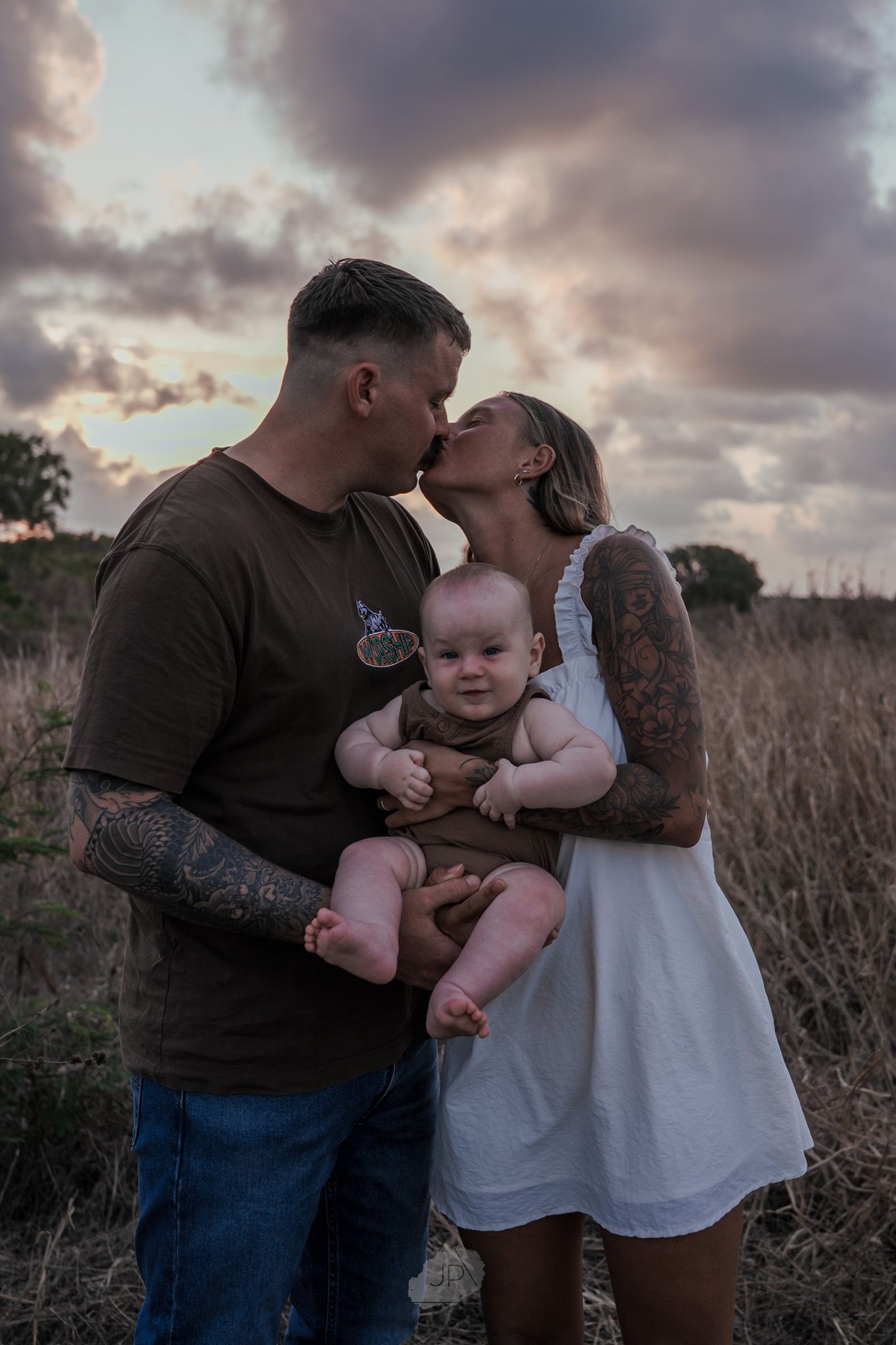 Family shares tender moments together during sunset photoshoot in a rustic field.