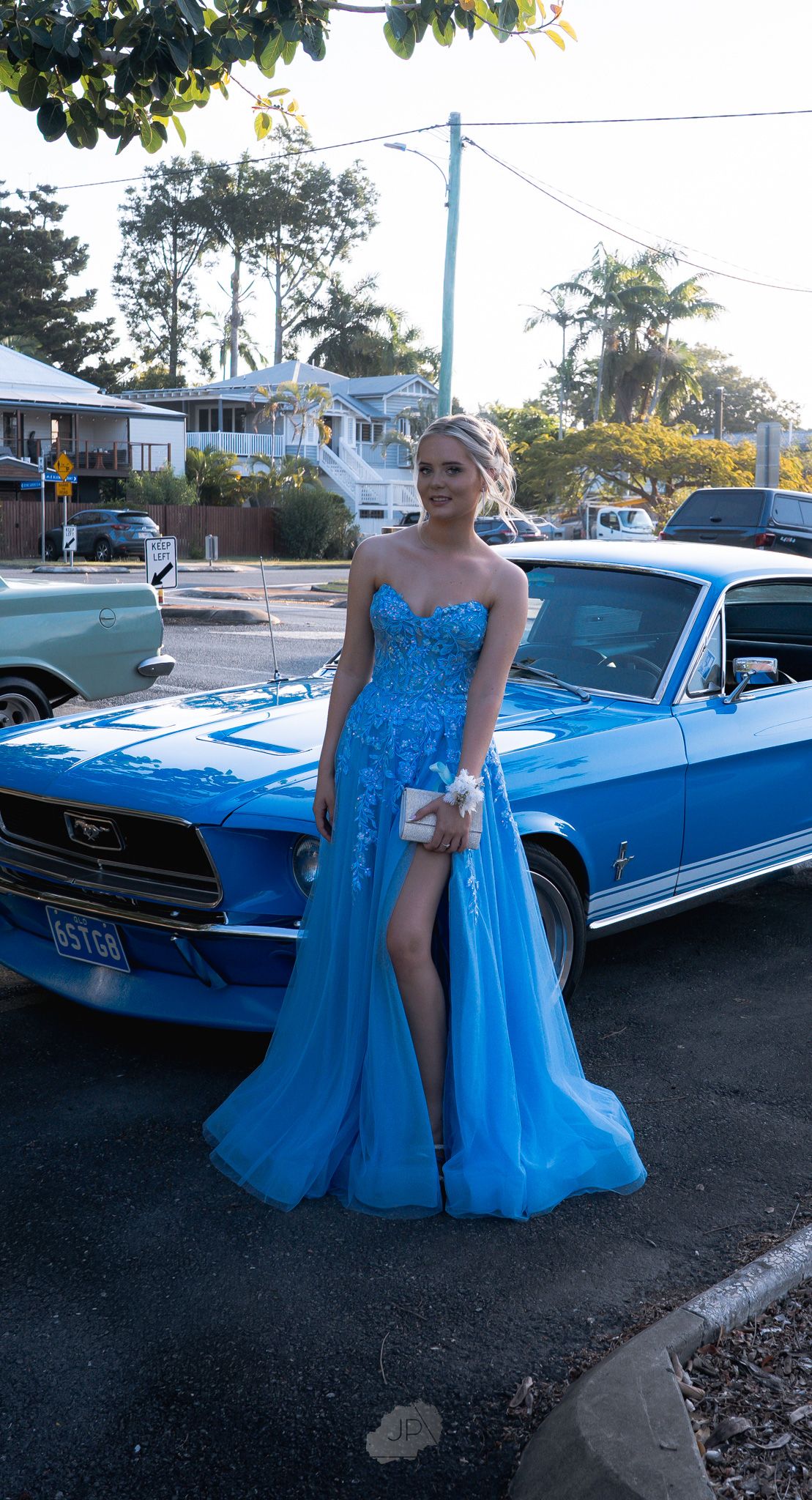A bright blue formal dress matches perfectly with a classic blue convertible car parked in an outdoor setting.