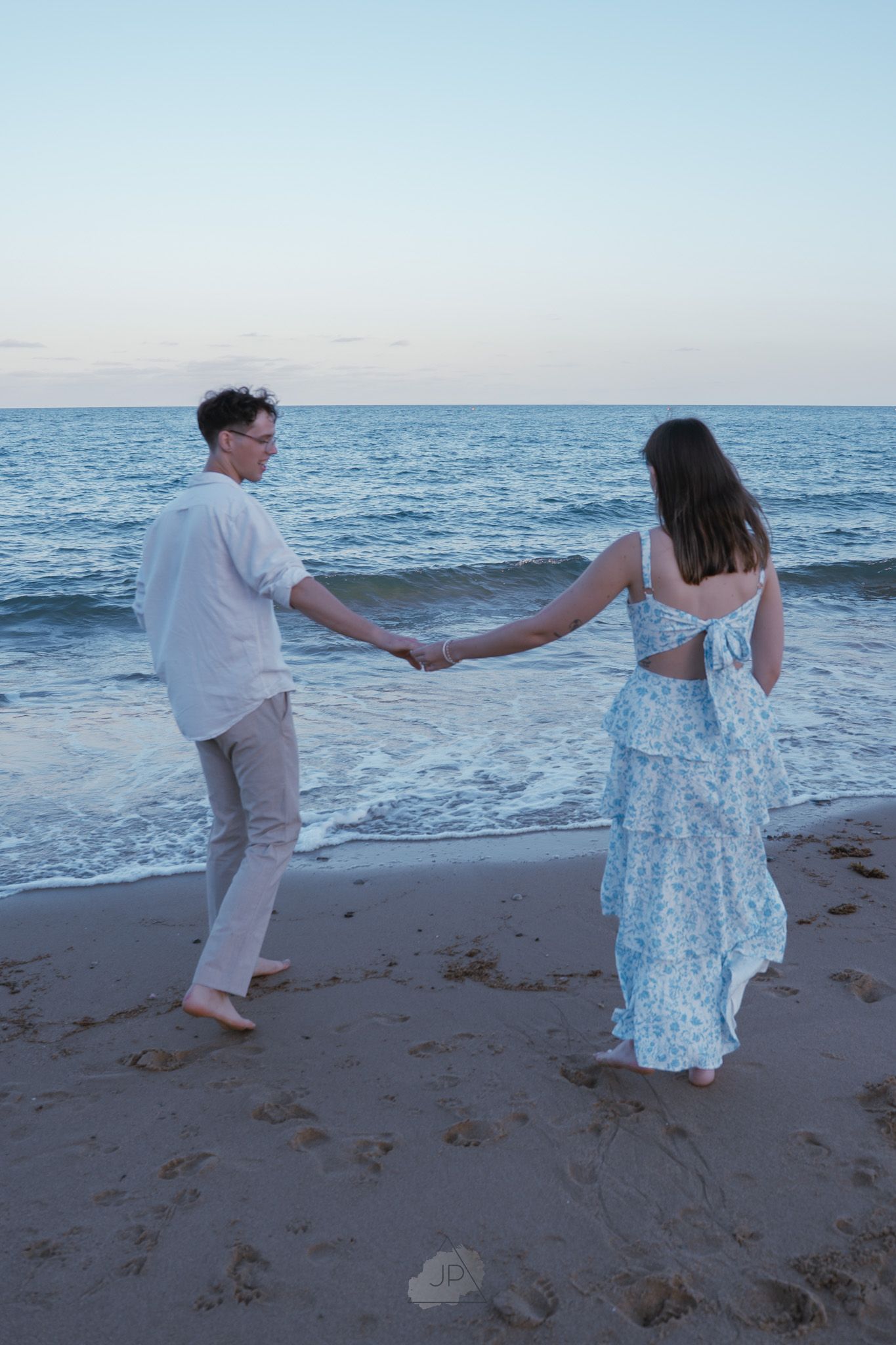 Couple dancing playfully together on a beach at sunset with ocean waves in the background.