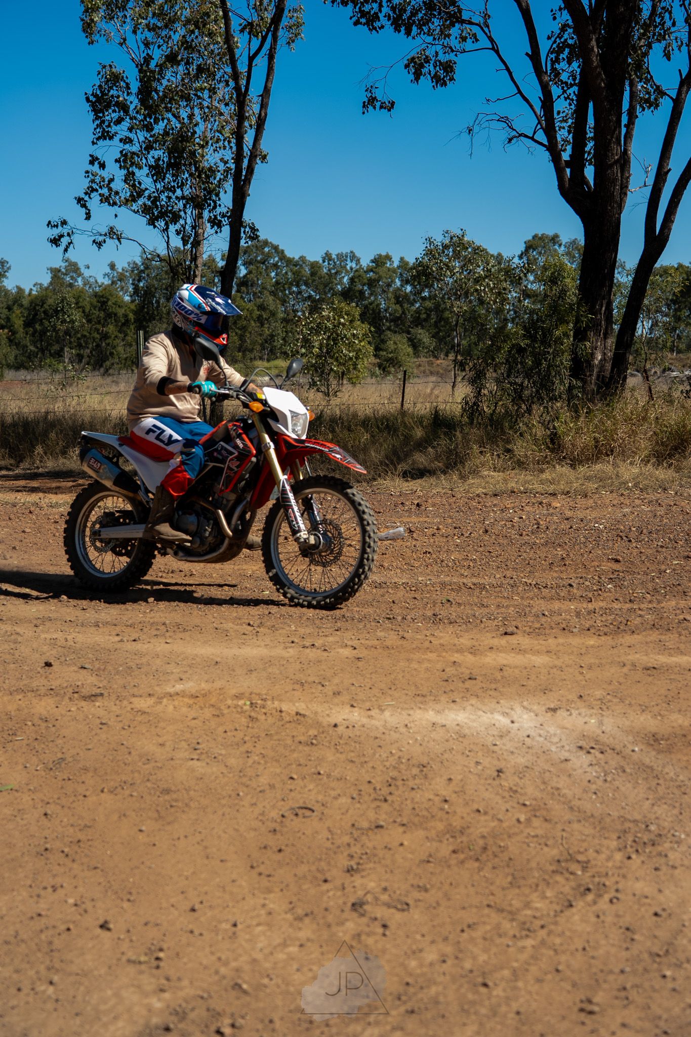 A KTM dirt bike parked on a dirt trail surrounded by trees and bushland in outback wilderness terrain.