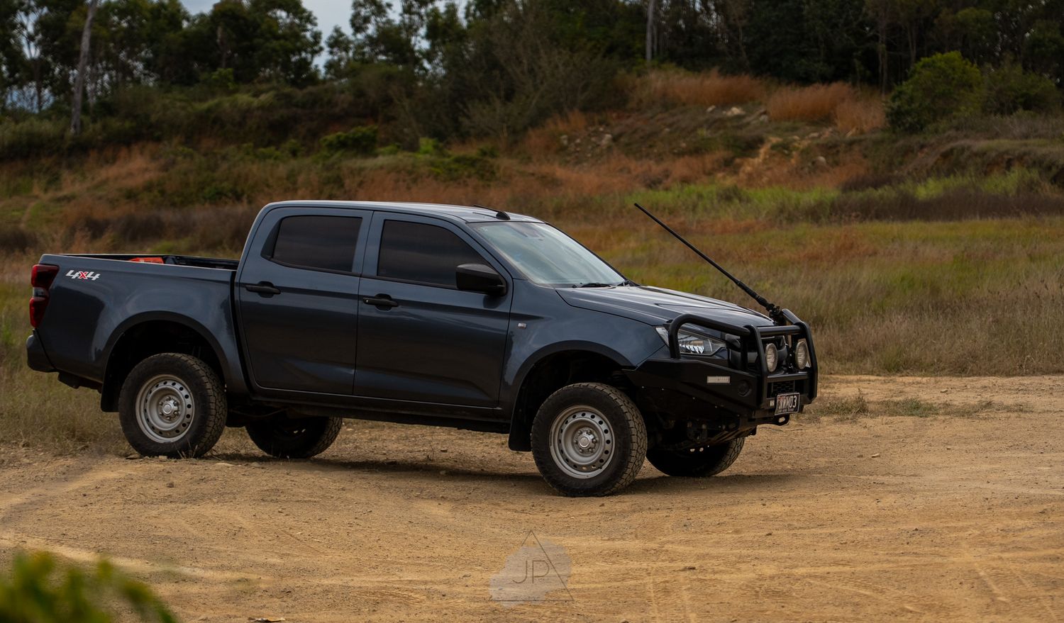 A line of black SUVs and pickup trucks parked on dirt terrain with hills in the background.