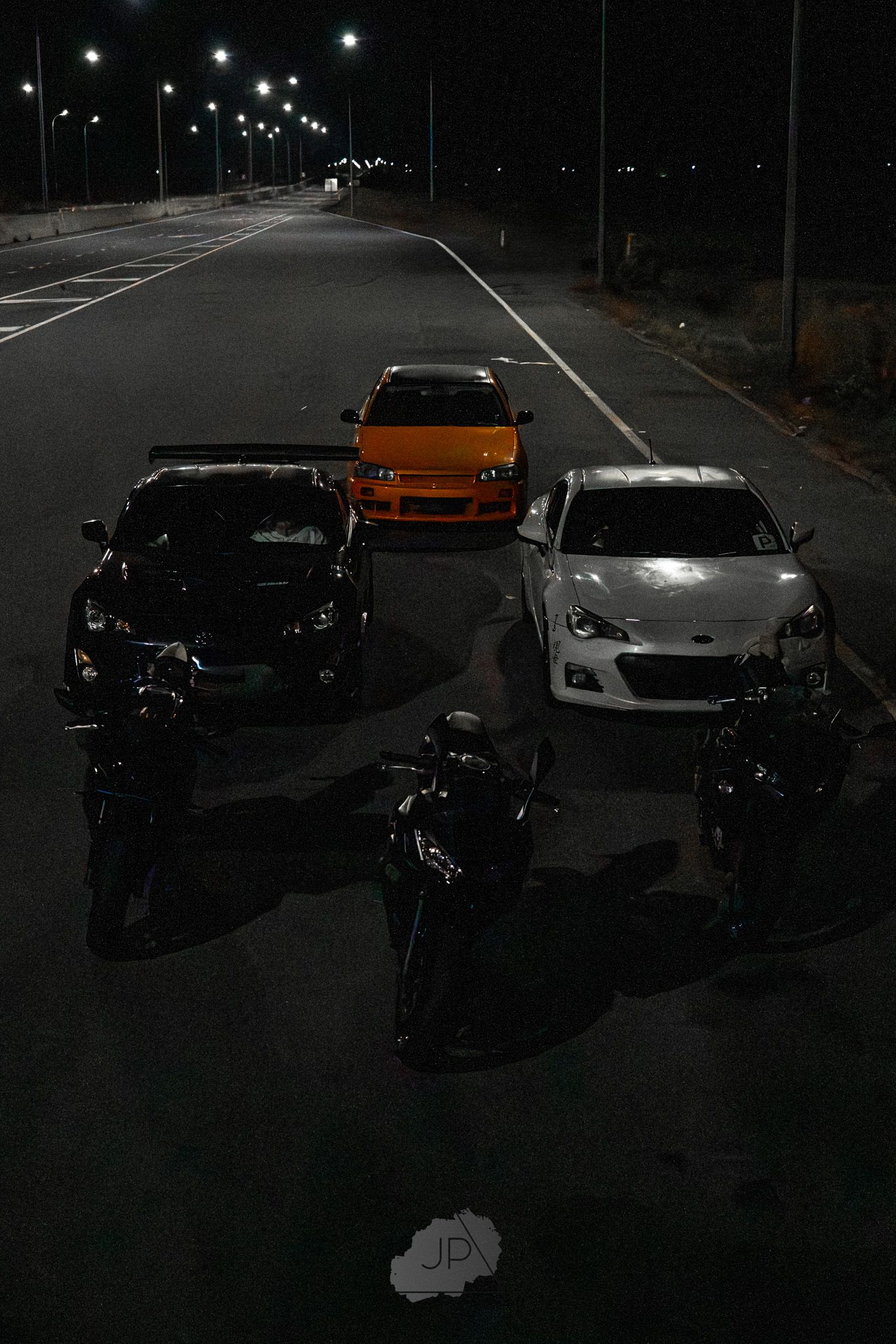 Performance cars parked in a dimly lit parking lot at night with street lights illuminating the scene.