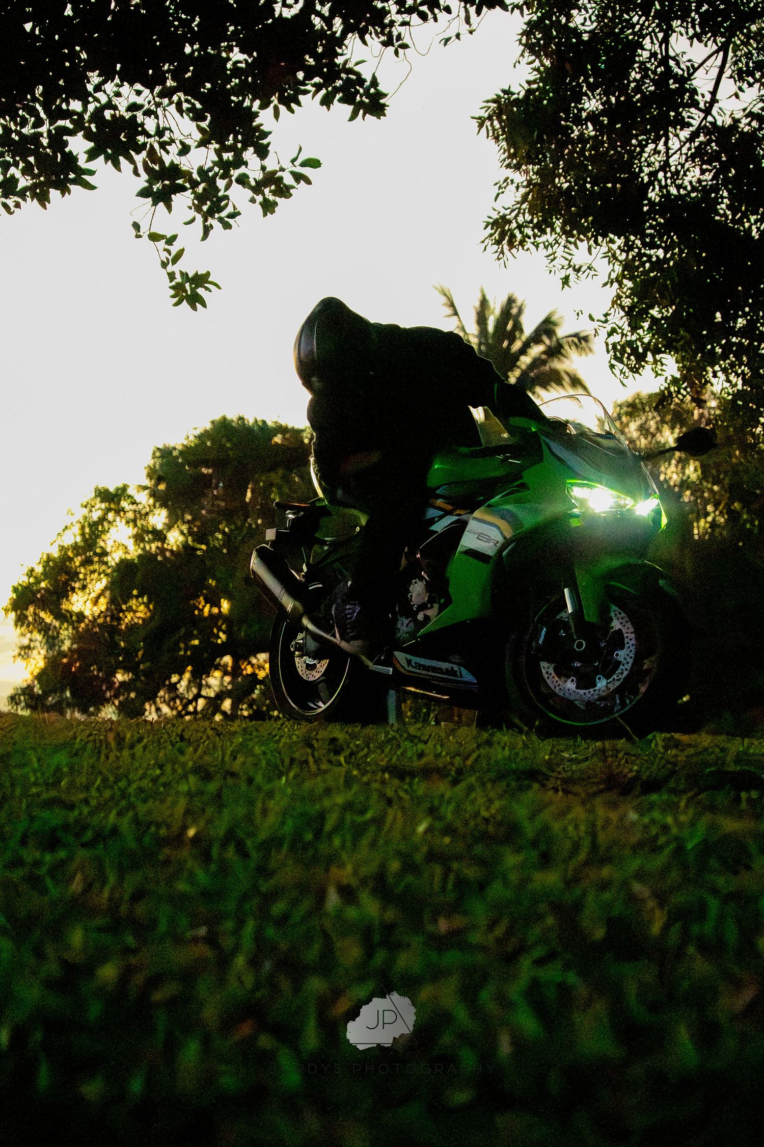 A green motorcycle silhouetted against a golden sunset in a grassy field during magic hour.