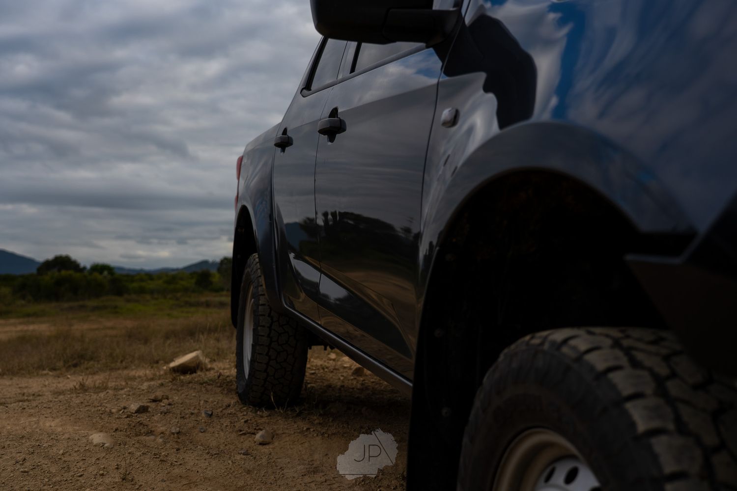 Black off-road pickup truck with lifted suspension and rugged tires shown from a side profile on a dirt path.