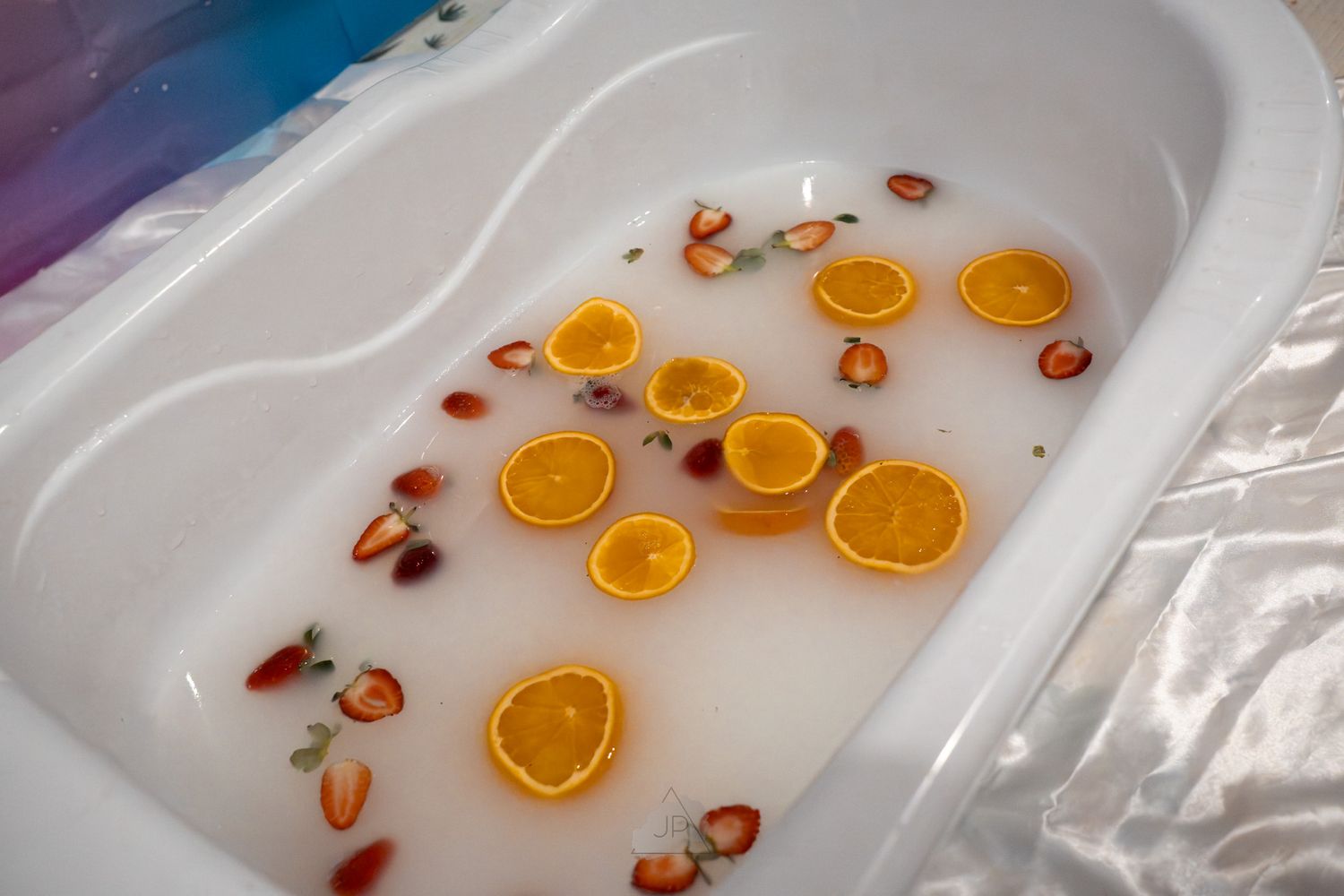 Sliced oranges and strawberries floating in a white bathtub filled with clear water.