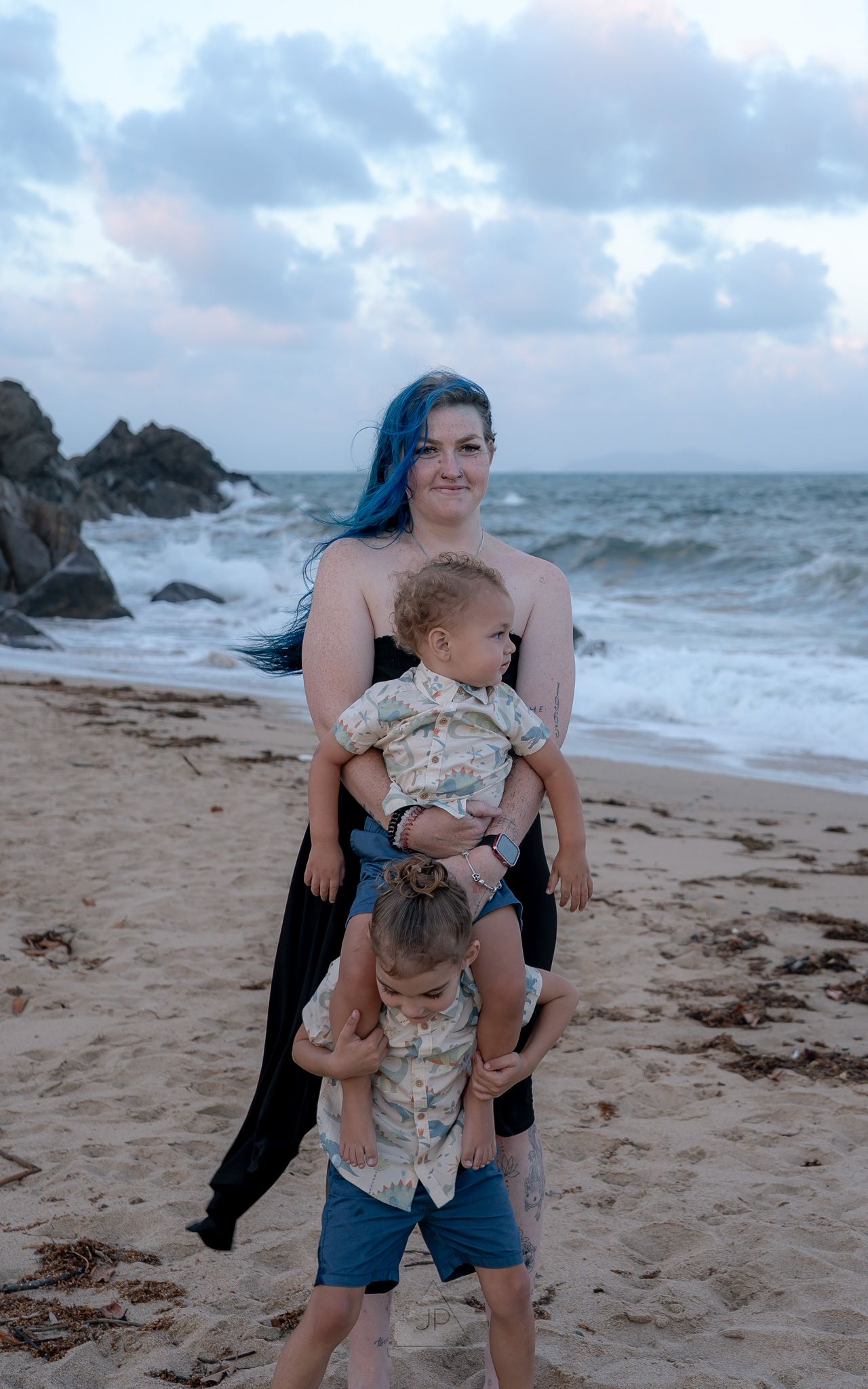 Family enjoying a beach day together with crashing waves and rocky coastline in the background.