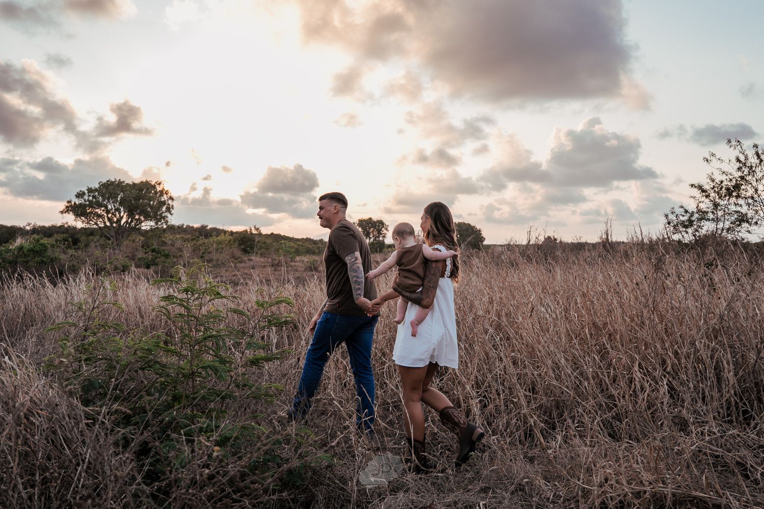 A couple stands in a golden field during sunset while holding hands and walking together.