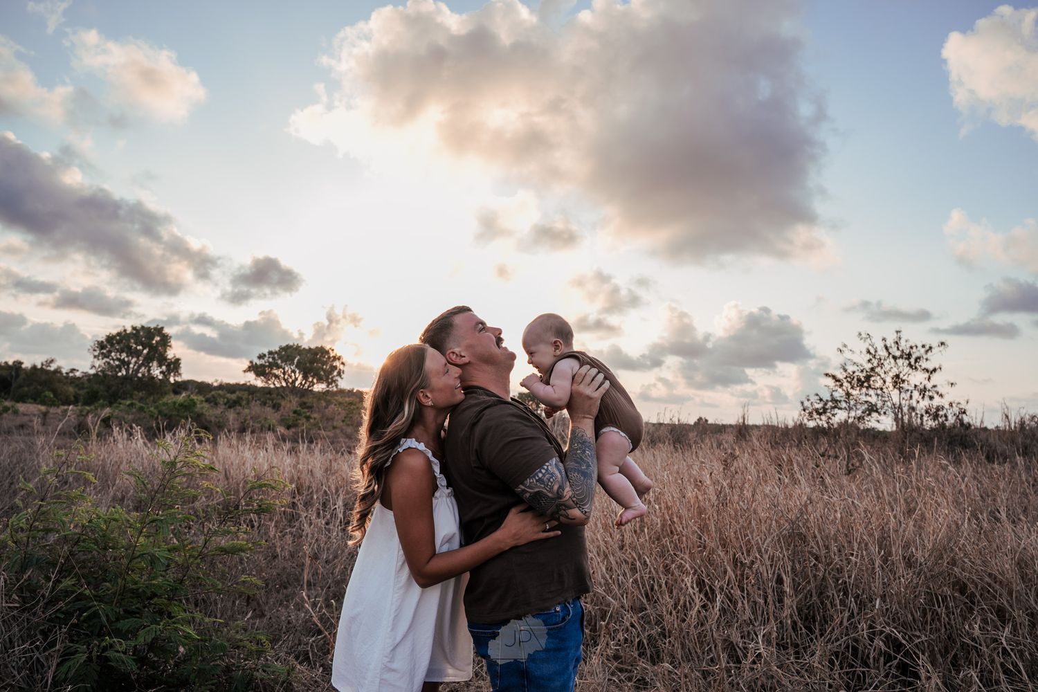A family embraces while standing in tall grass during golden hour.