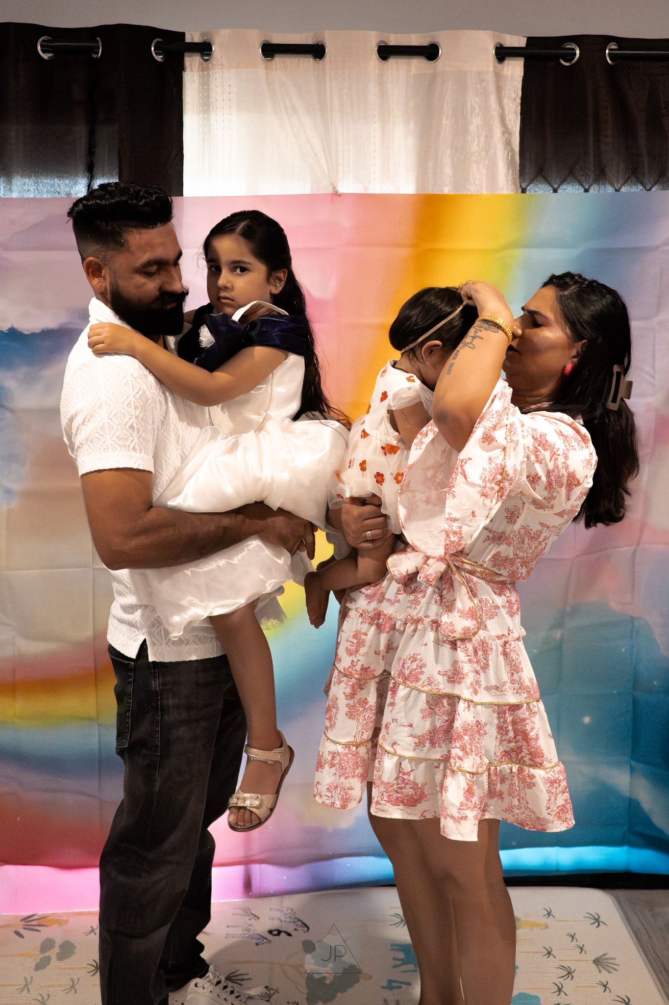 A couple performs dance moves in matching outfits against a rainbow-colored wall with artistic lighting.