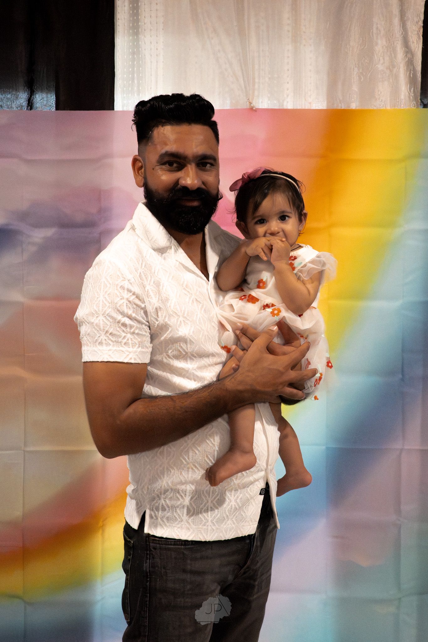 A sequence of photos showing someone in a white shirt and dark pants holding a small baby against a colorful background.