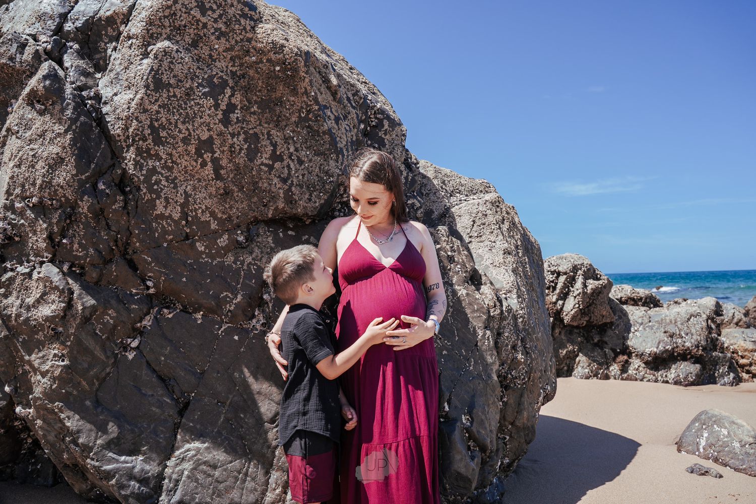 A series of coastal rock formations with a person in a pink dress exploring the rocky beach landscape.