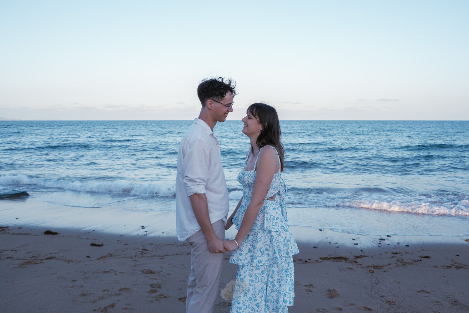 A romantic couple shares a tender moment on the beach at sunset with ocean waves in the background.