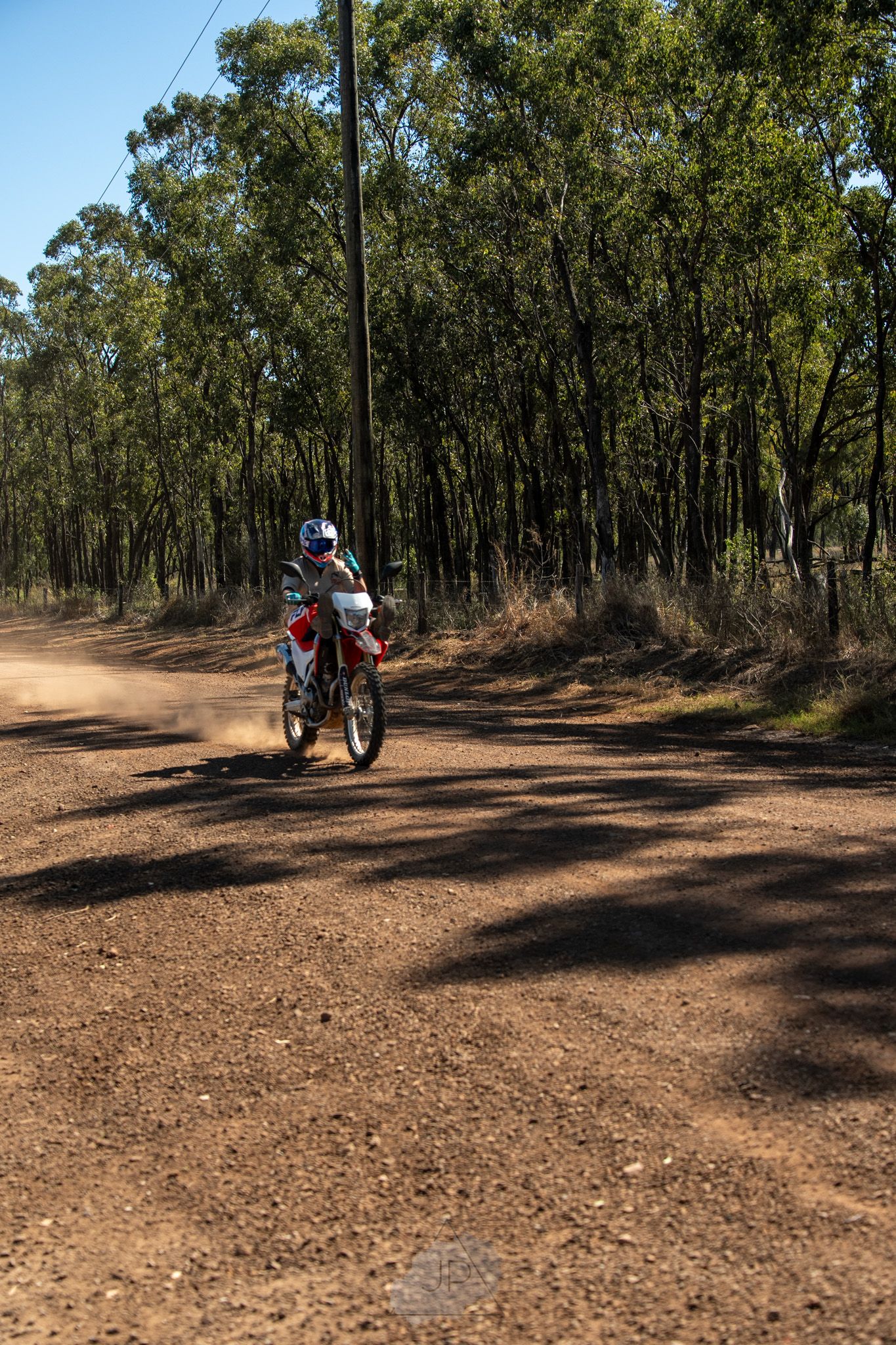 A dirt bike rider navigates a dusty trail through eucalyptus forest on a sunny day in Australia.