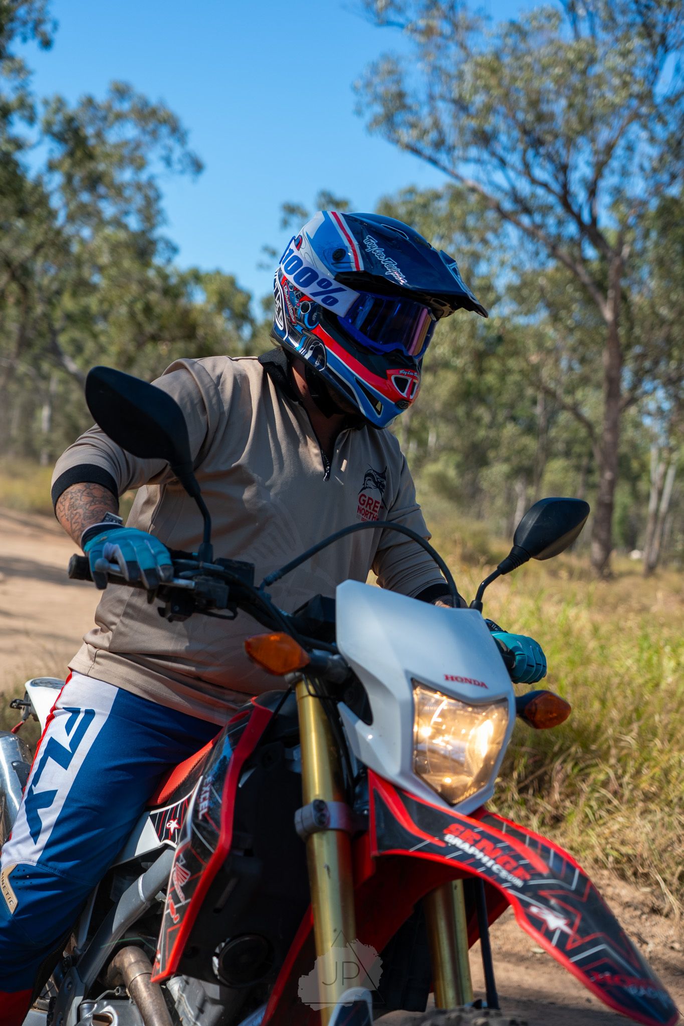 A close-up shot of a dirt bike rider on a red motorcycle with blue gear against a natural outdoor background.