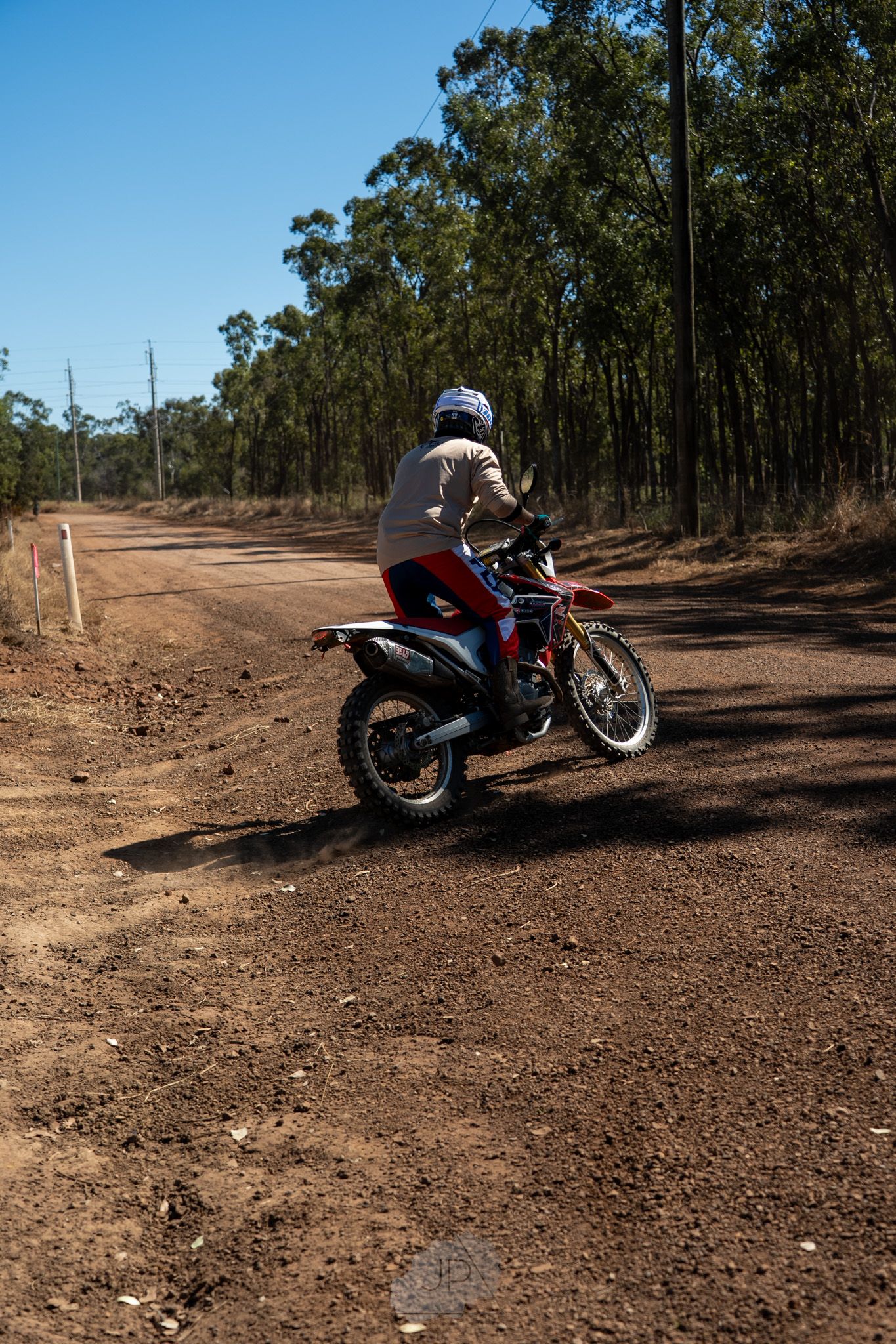 A red motorcycle parked on a dirt trail surrounded by eucalyptus trees in the Australian outback, shown from multiple angles.