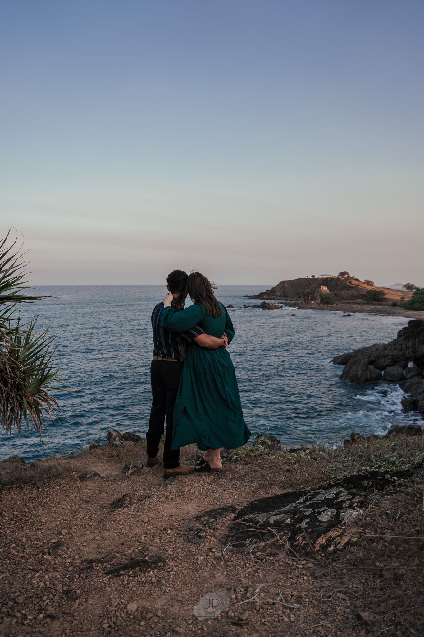 Couple enjoying a romantic sunset moment on rocky coastal cliffs overlooking the ocean.