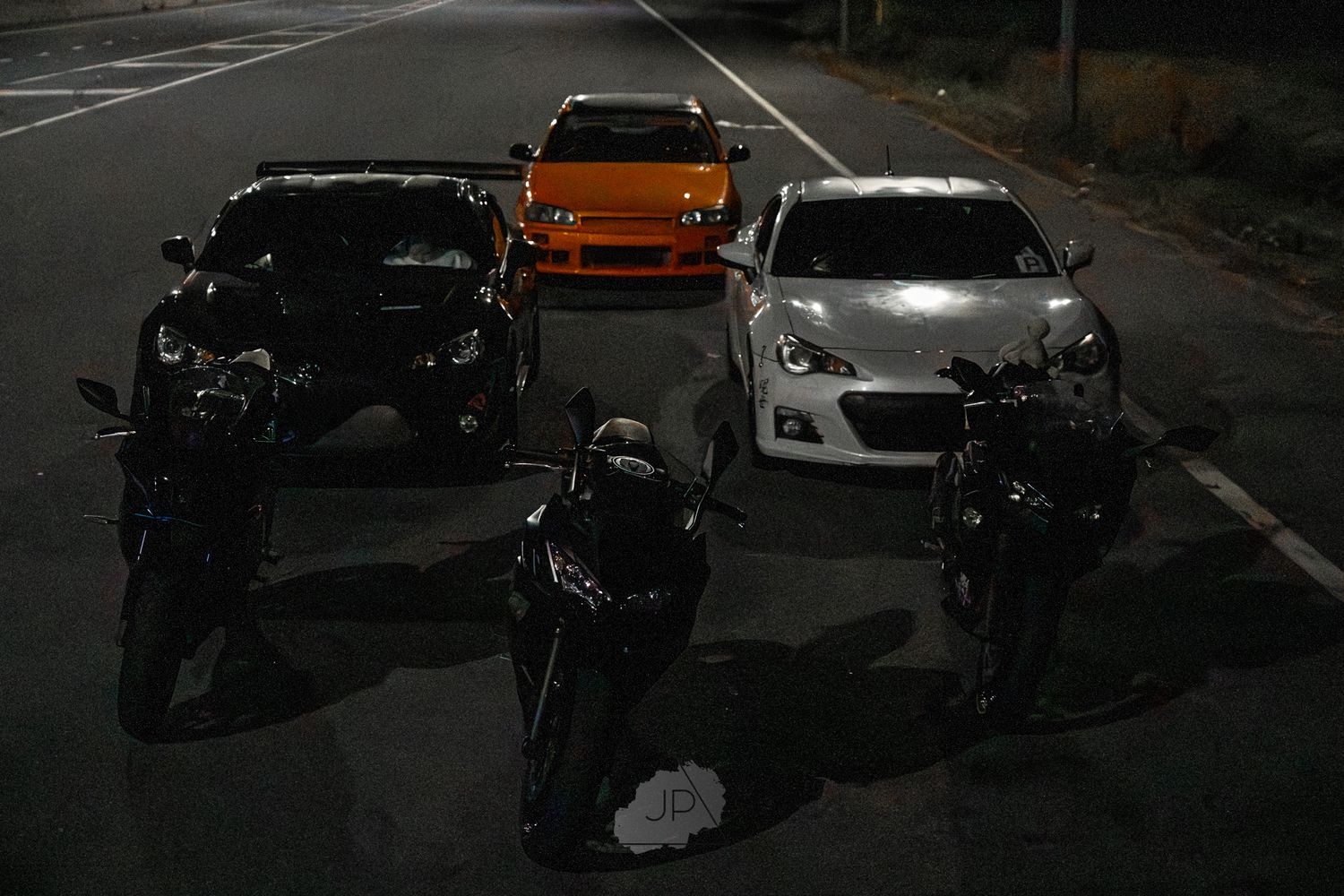 Dark parking lot at night with multiple parked vehicles and orange truck visible in the background.