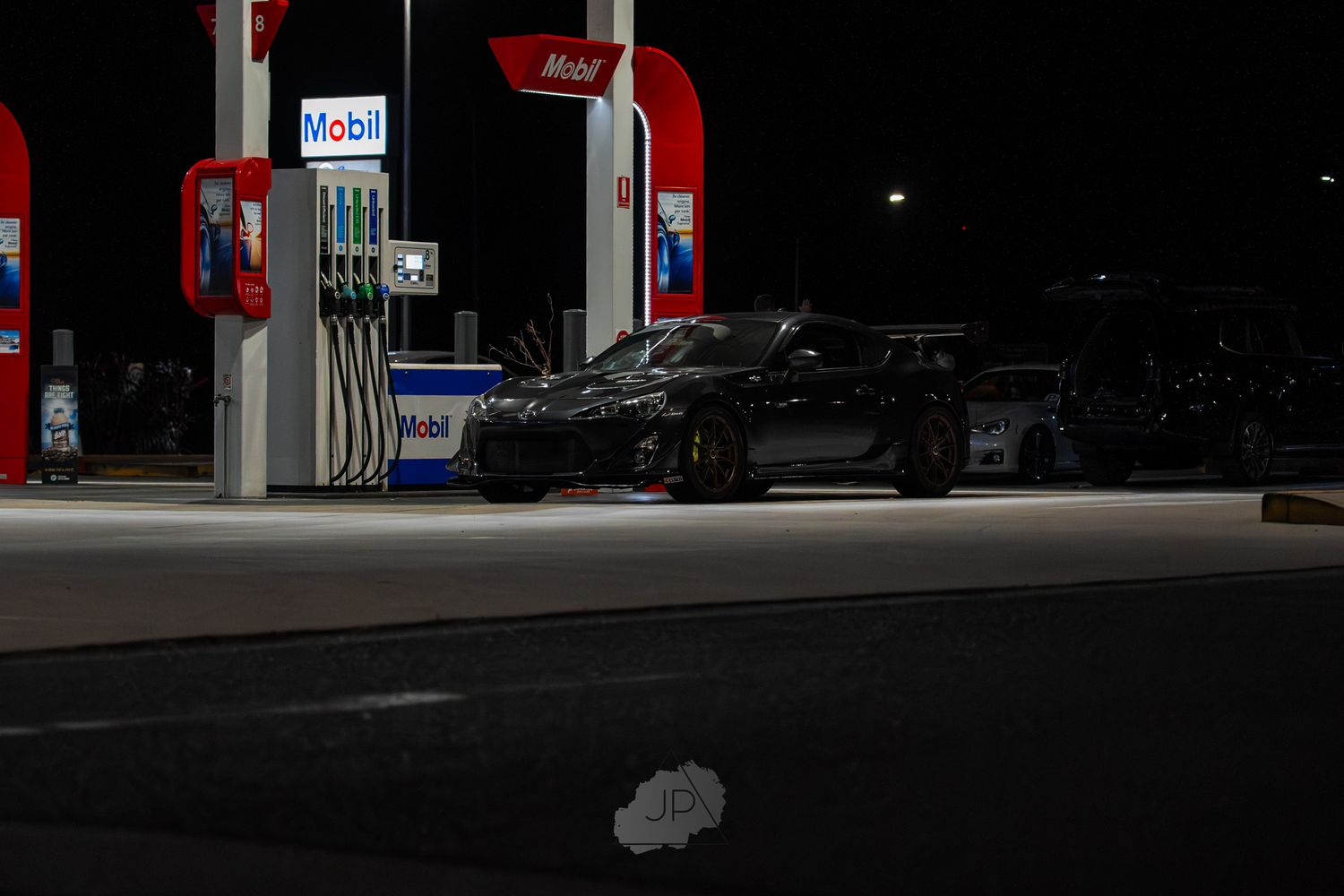 Gas station pumps illuminated at night with red signage and dark surroundings creating a moody atmosphere.