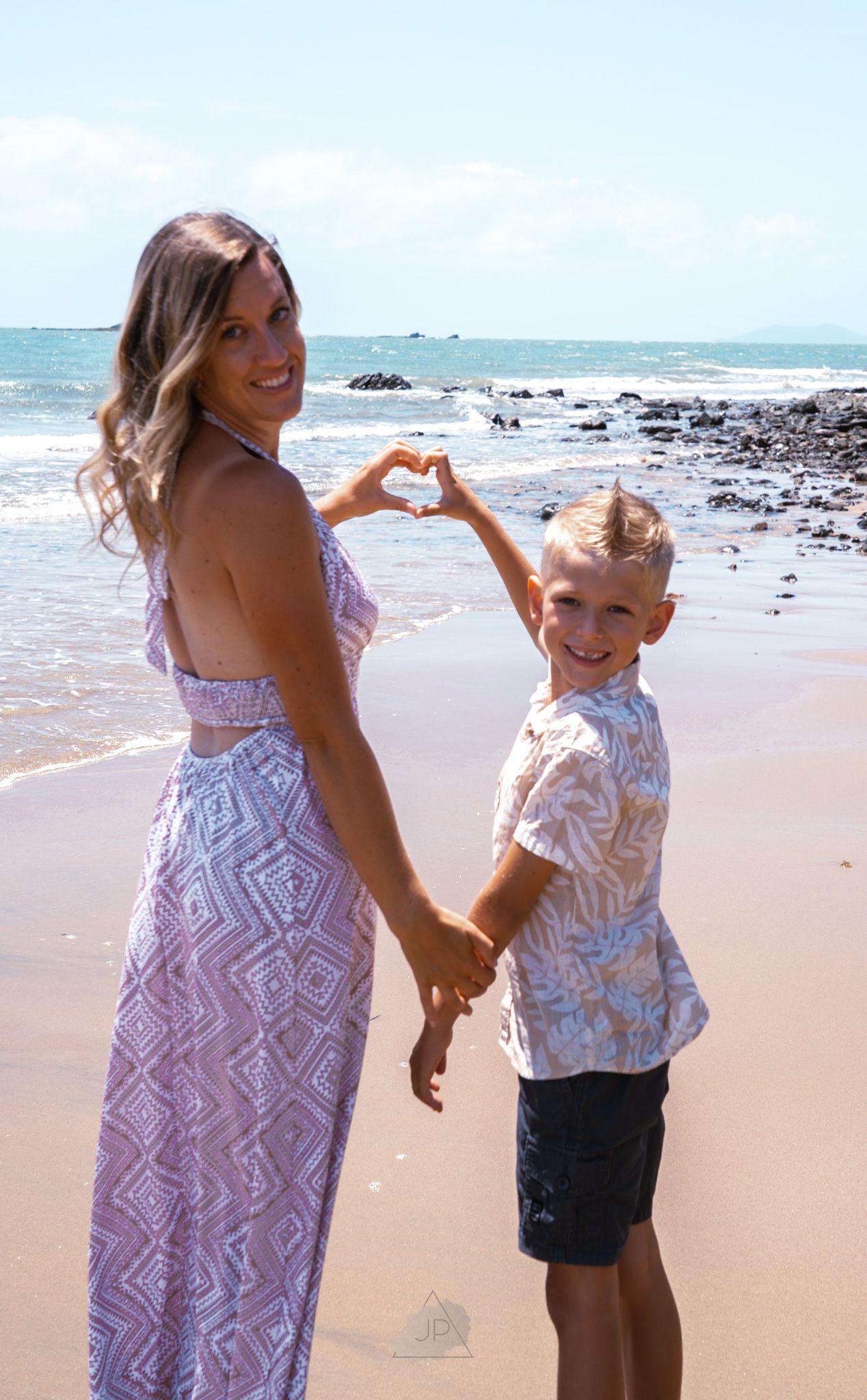 A parent and child share a joyful moment together while playing on a sunny beach with ocean waves in the background.