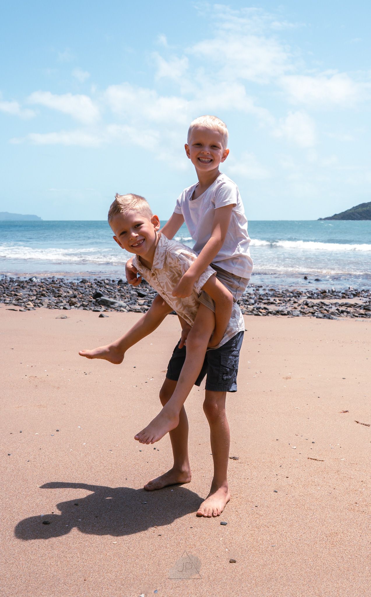 Two children playing and having fun together on a sandy beach with ocean waves in the background.