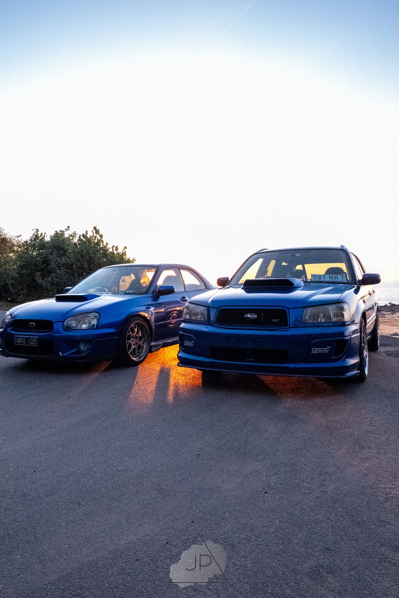 Modified blue Subaru Impreza cars lined up at dusk showcasing their lowered stances and sleek profiles.