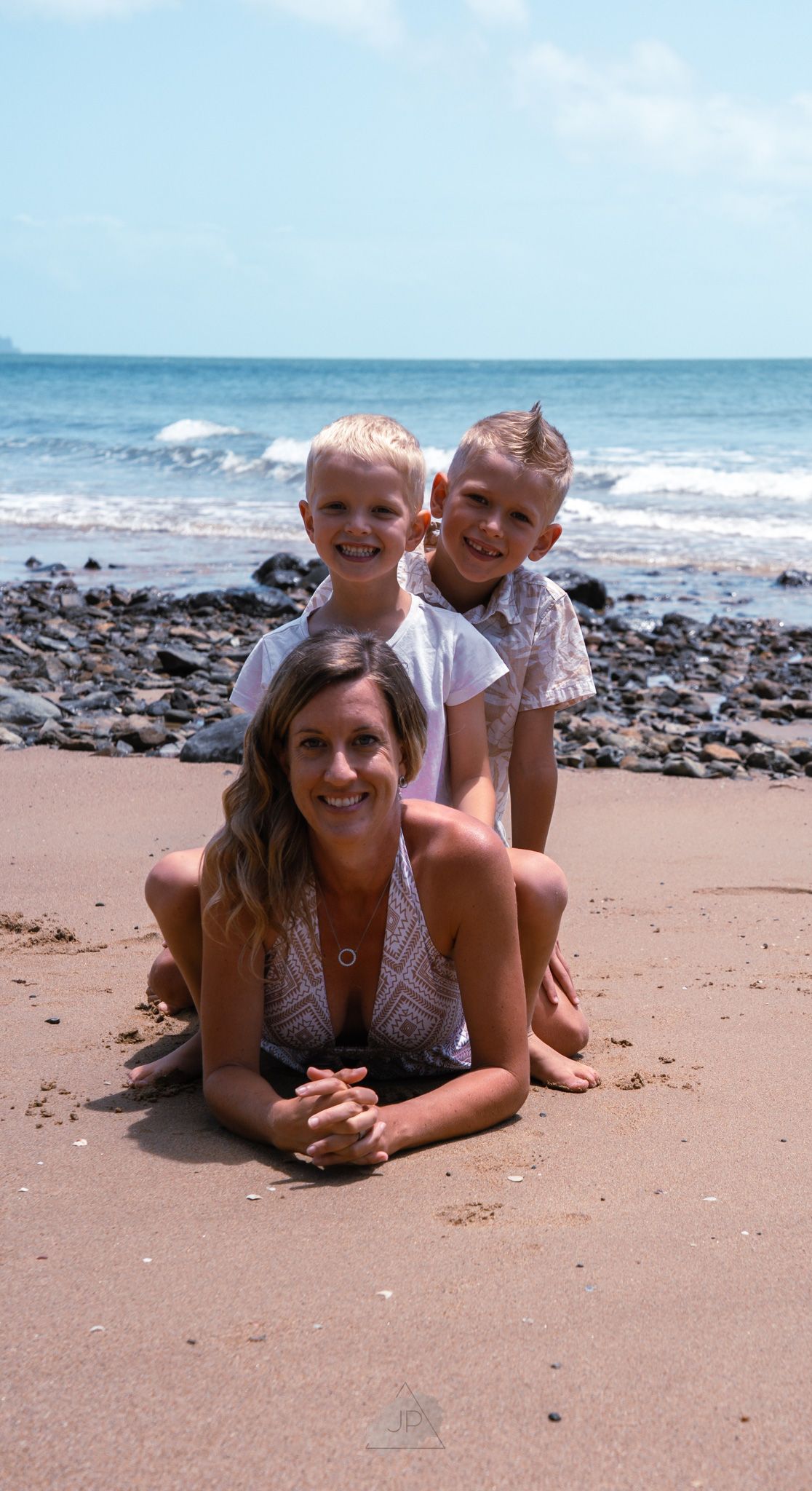 A group relaxes together on a sandy beach with rocky shoreline and ocean waves in the background.