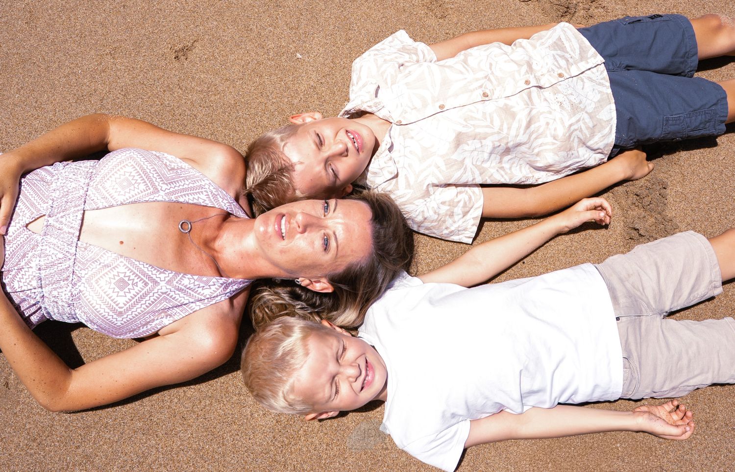 Three people lying on a carpeted floor in casual clothing, smiling and relaxing together.