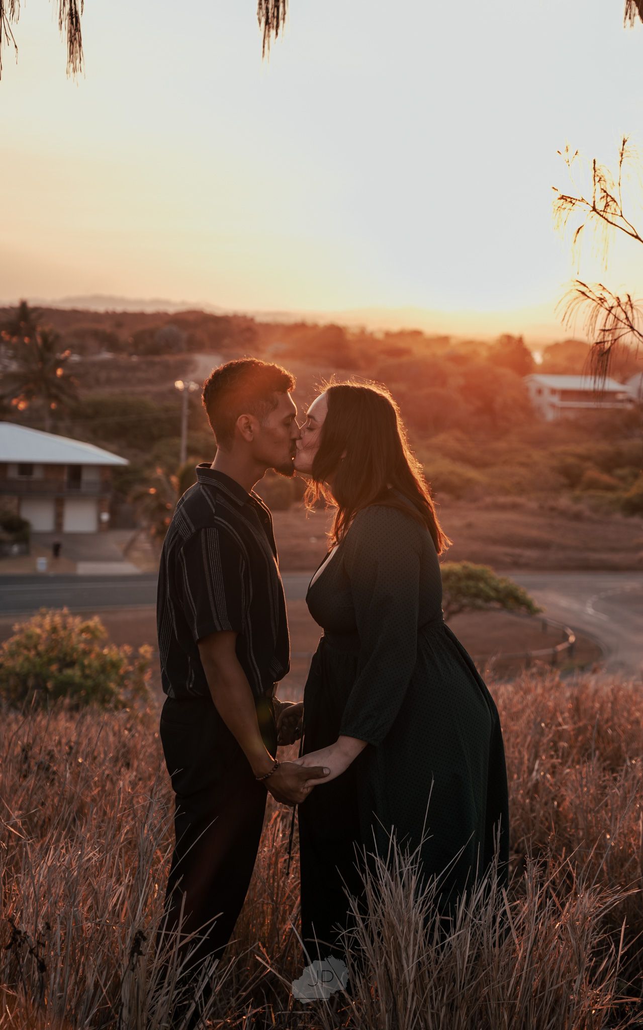 A couple shares a romantic moment in a field during golden hour sunset, creating a warm and intimate silhouette.