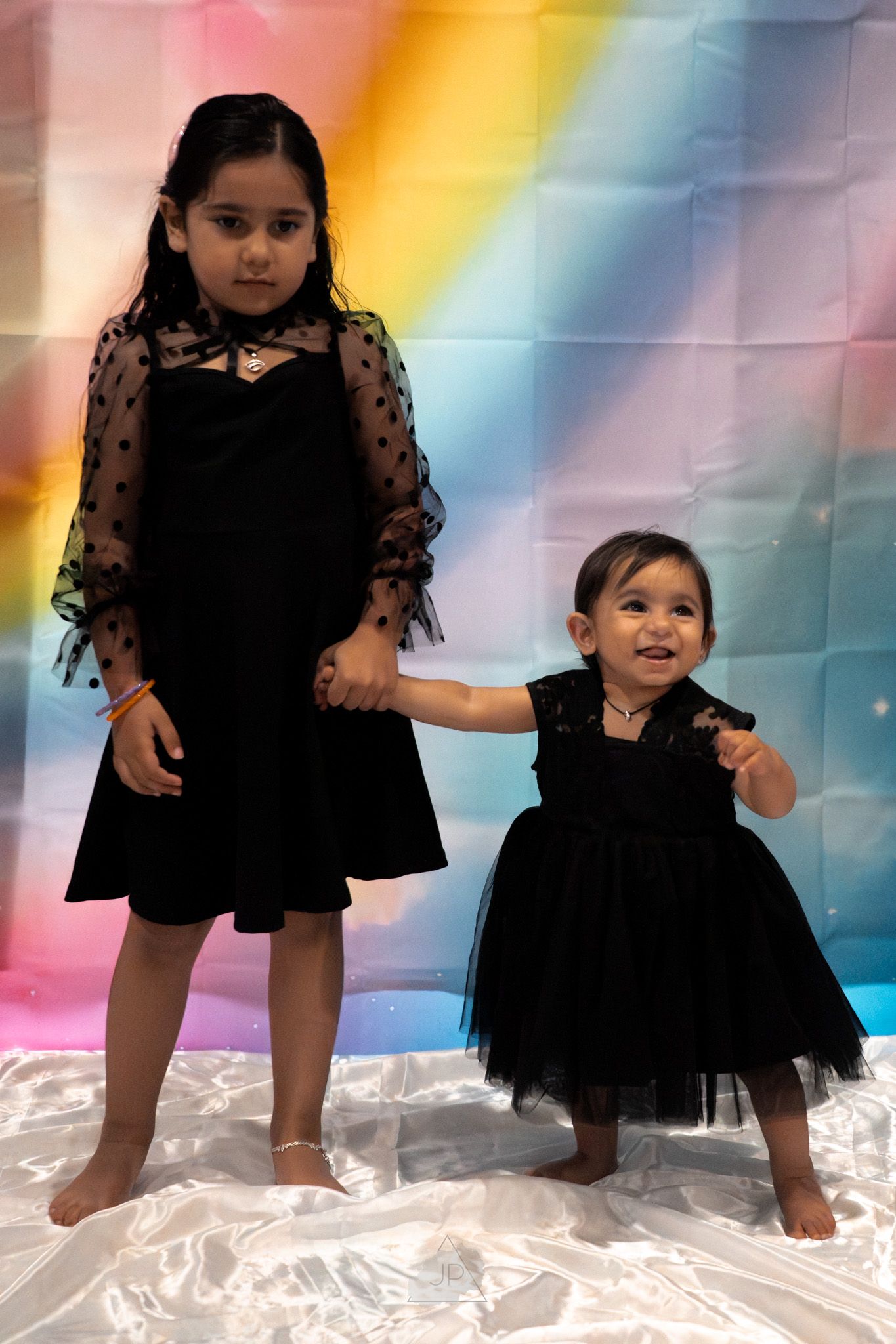 A sequence of five photos showing a child in a black dress dancing and twirling against a colorful rainbow backdrop.
