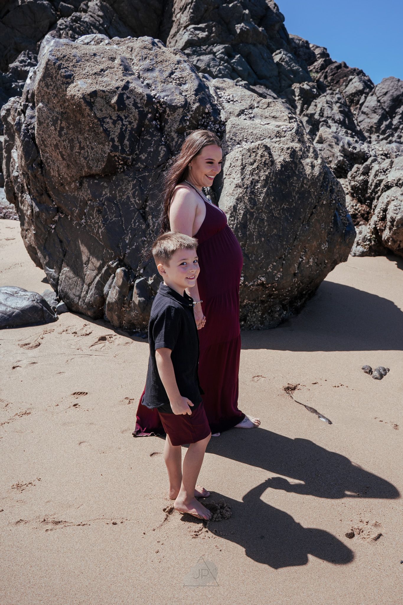 A series of photos showing two people posing near large coastal rocks on a sandy beach in coordinated outfits.