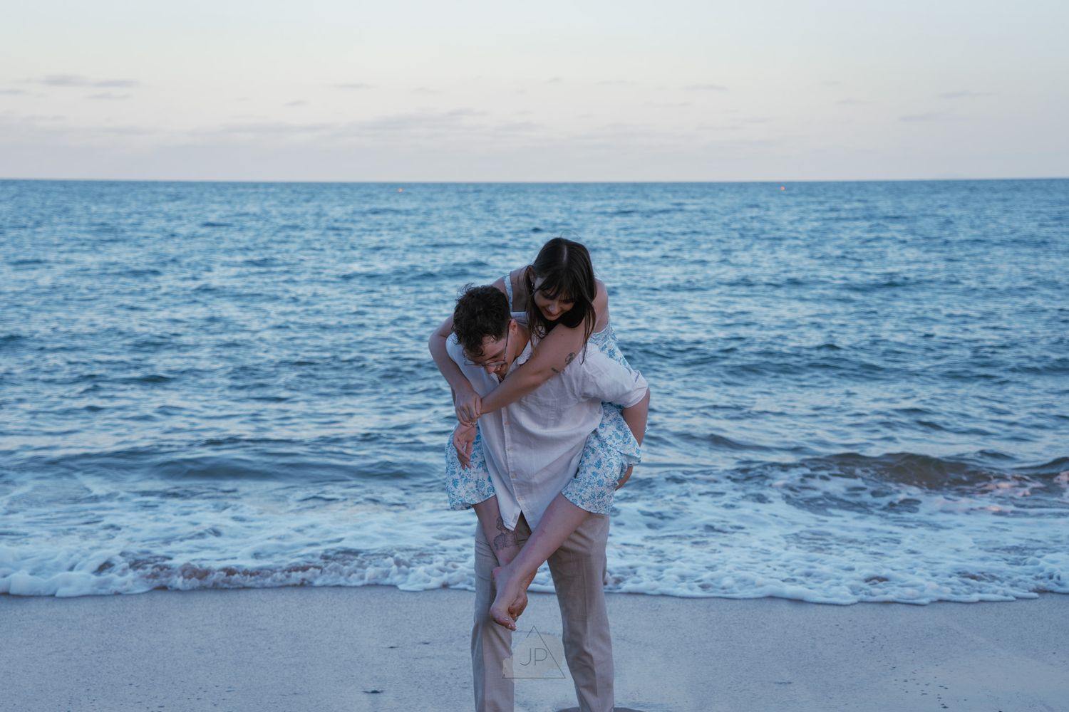 Person in white dress walks along the ocean shore during sunset, creating a serene coastal scene.