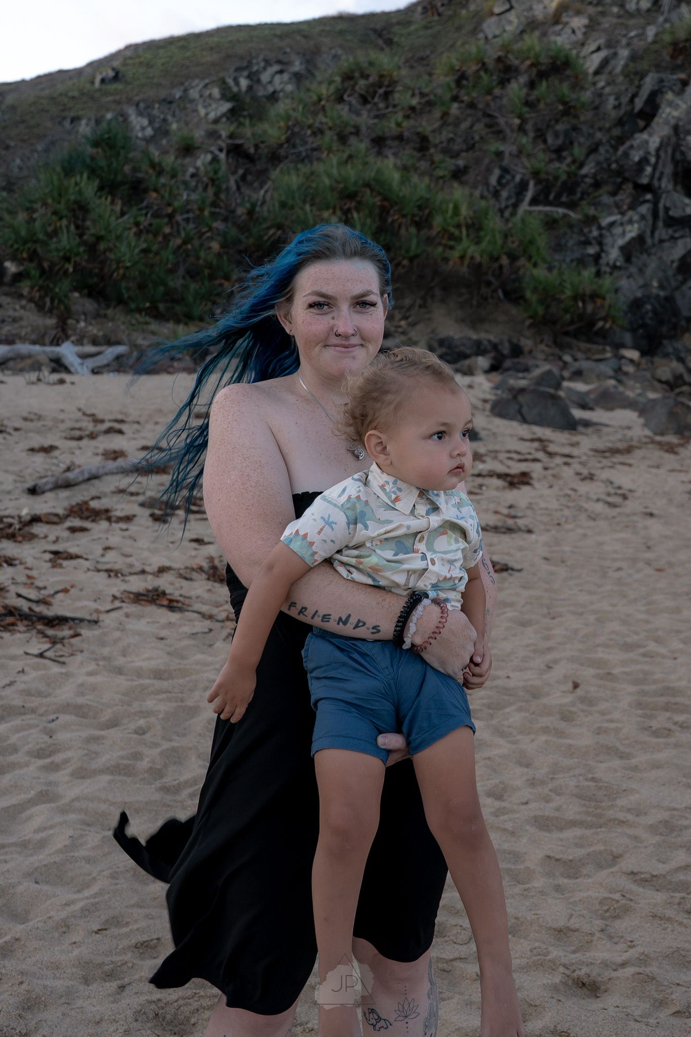 A parent and child share a tender moment together on a sandy beach with rocky cliffs in the background.