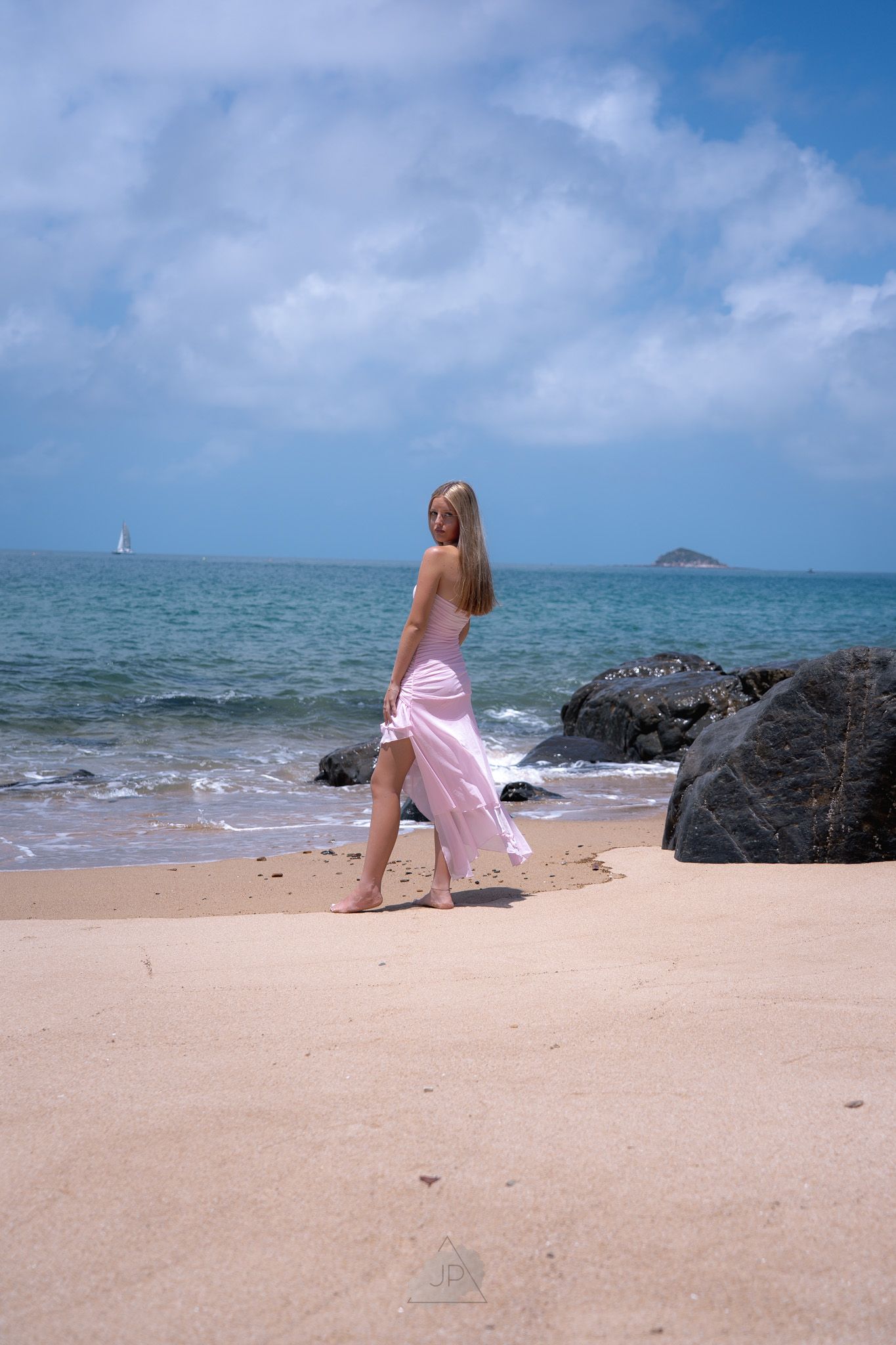 Person in pink dress explores rocky beach shoreline with turquoise ocean and blue sky in Hawaii.