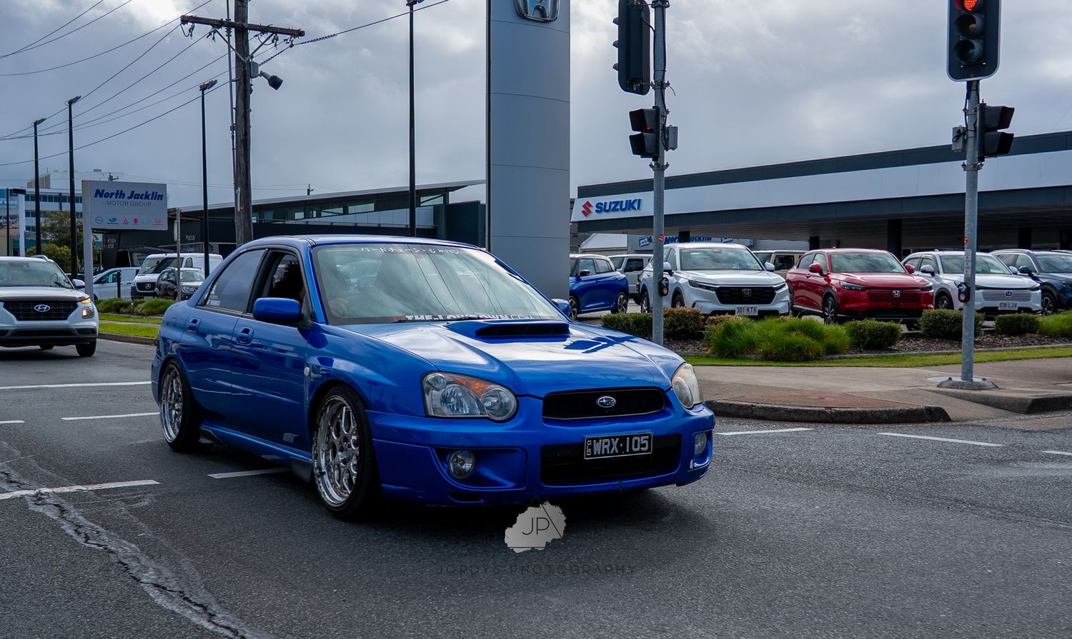 A blue Subaru WRX STI sports car parked by a traffic light intersection during an overcast day.