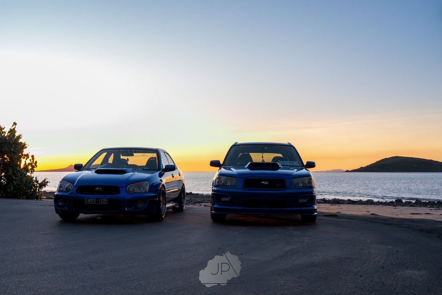 Blue BMW M4 sports cars lined up against a scenic sunset backdrop at the oceanfront.