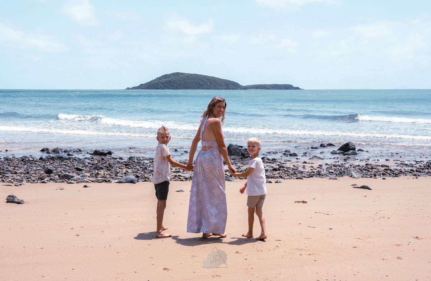 Family enjoying a sunny day at the beach with waves crashing and rocky coastline in the background.