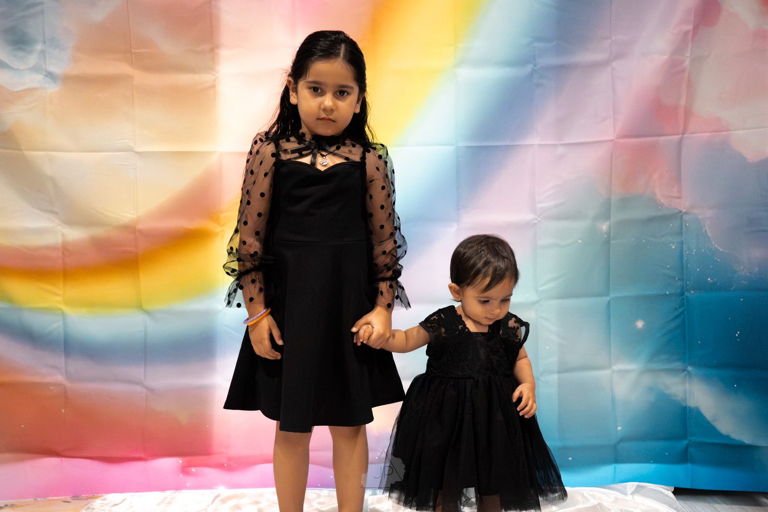 Two children in matching black outfits pose in front of a colorful backdrop during a photo session.