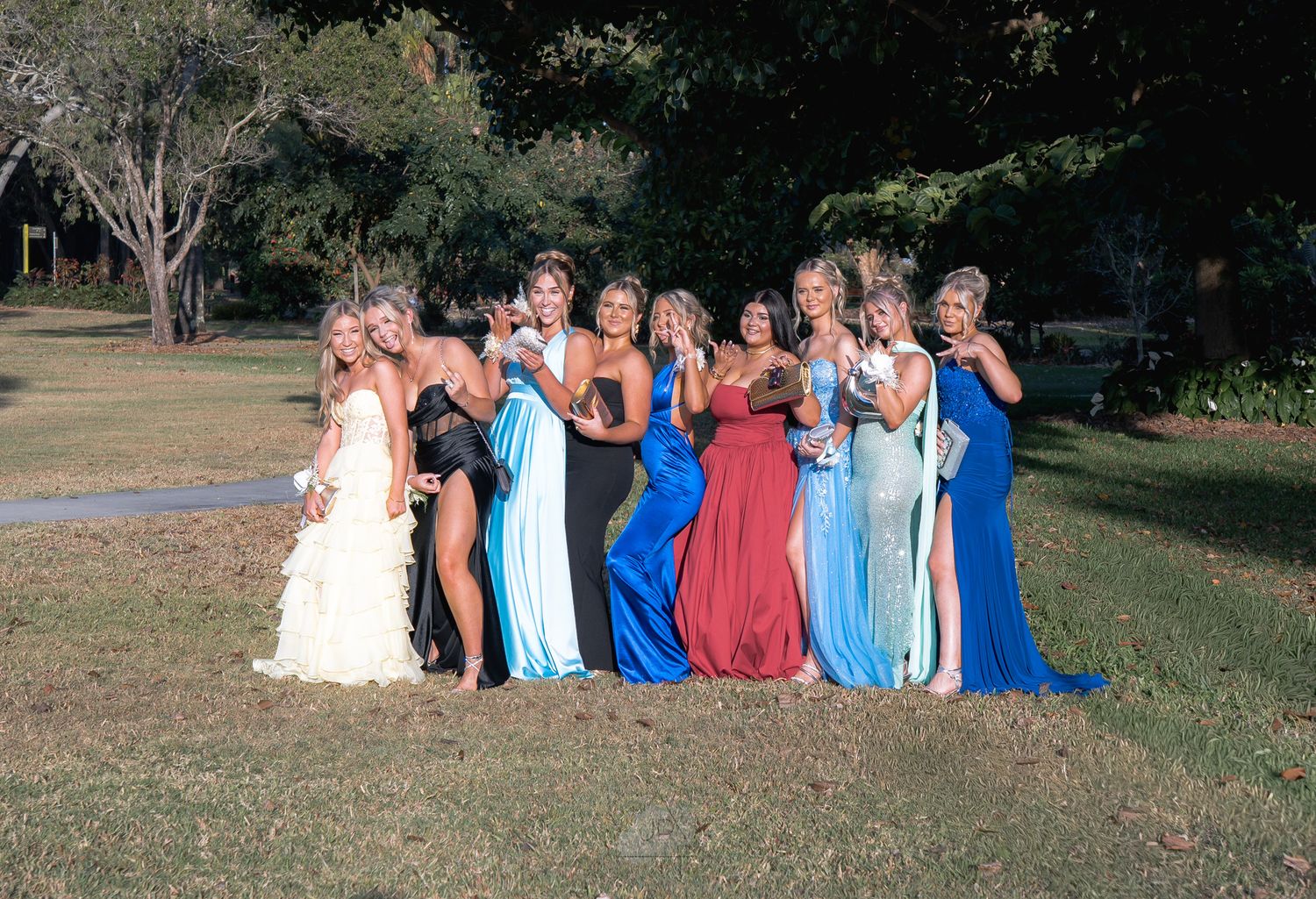 A group in formal attire poses together outdoors in a grassy area during sunset.