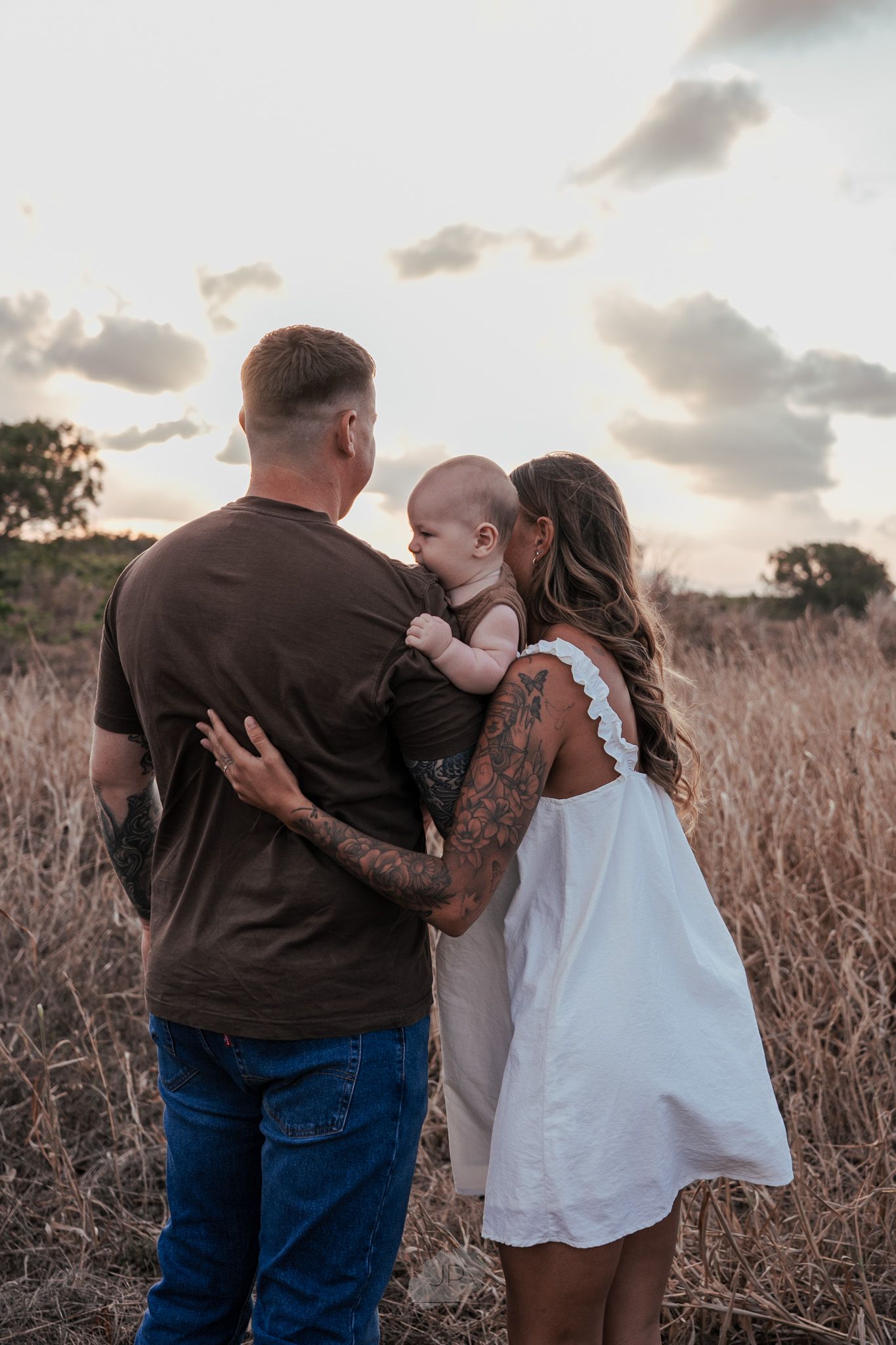 A loving family embraces together in a golden wheat field at sunset.