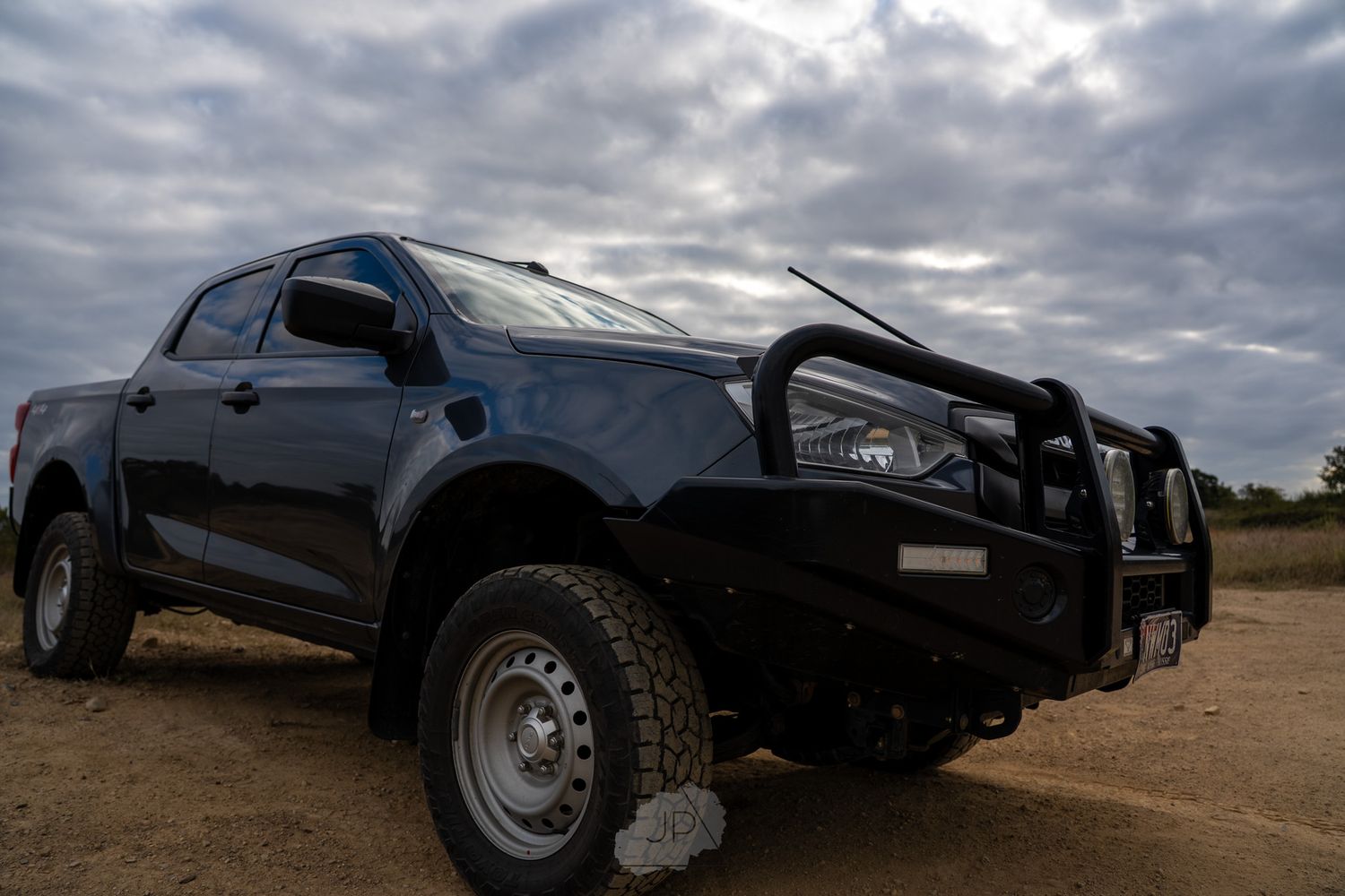 Low angle view of a black off-road truck parked on a dirt trail against a dramatic cloudy sky.