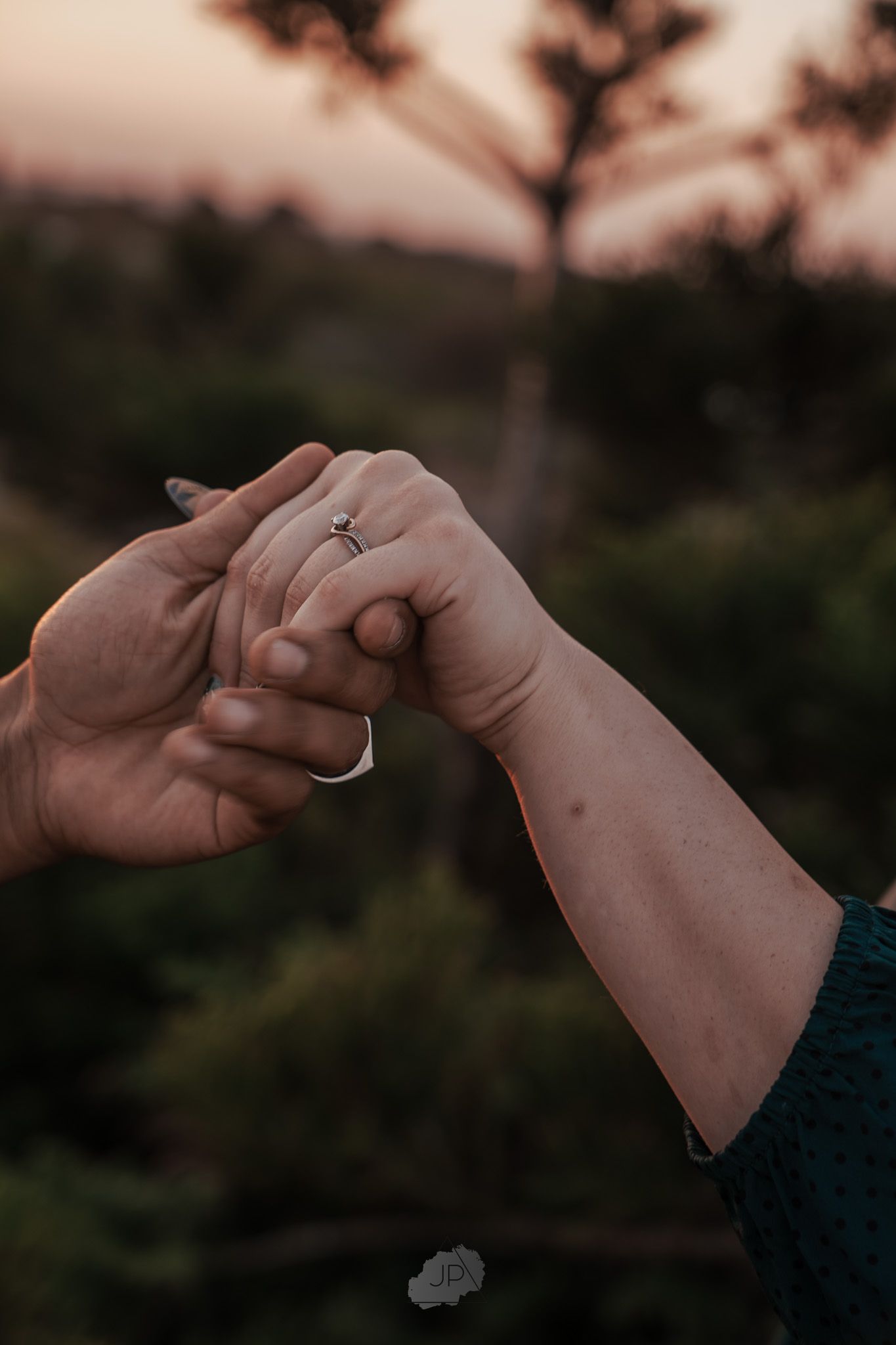Close-up of hands with engagement ring during sunset proposal photoshoot.