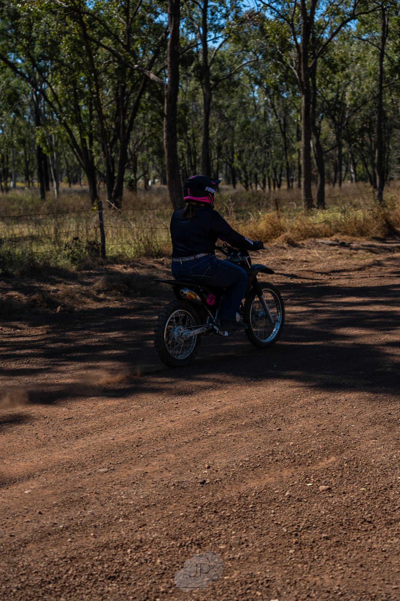 A dirt bike rider traverses a winding trail through a wooded forest area on a sunny day.