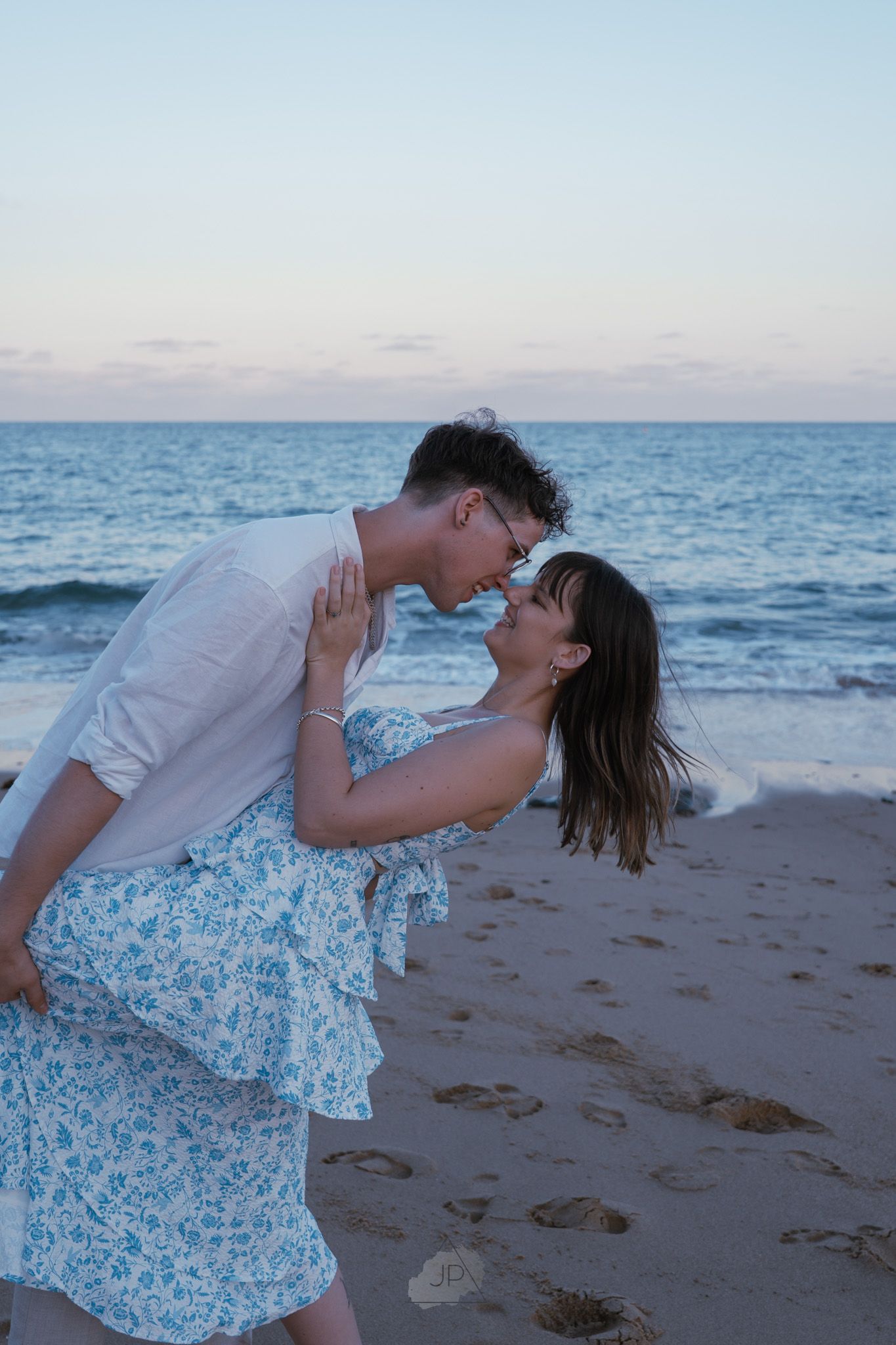Couple embraces and dances together on sandy beach with blue ocean waters stretching to the horizon.