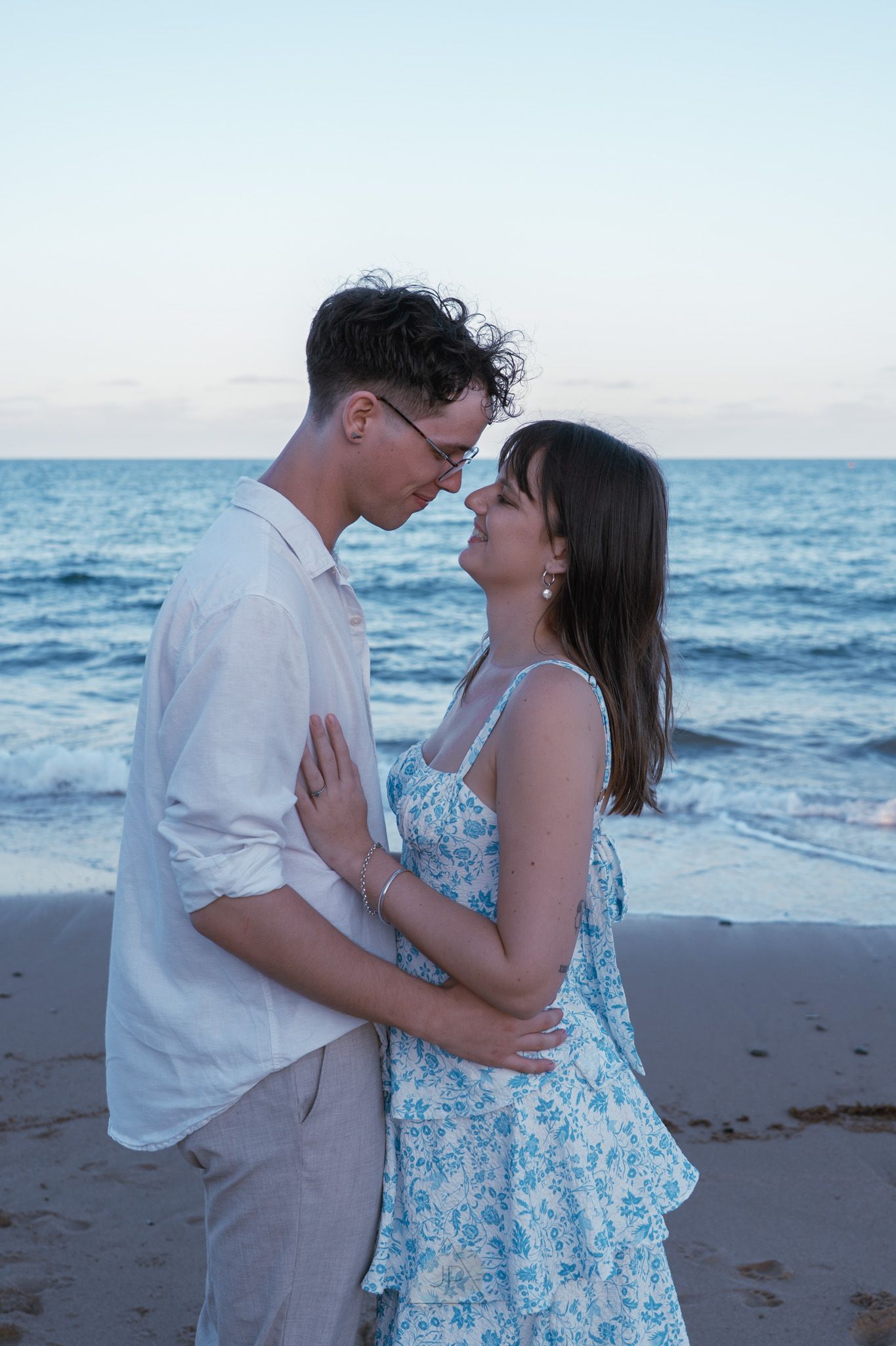 A couple shares romantic moments on a beach at sunset with the ocean waves in the background.