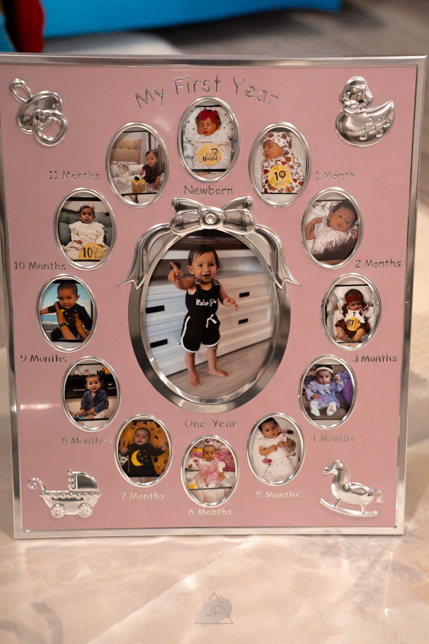 A pink 'My First Year' photo frame with twelve monthly milestone photos arranged around a larger central image.