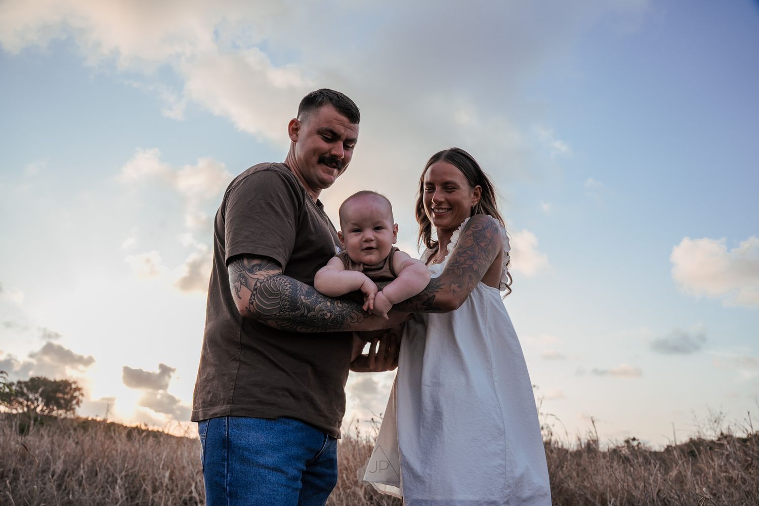 A family stands together in a field at sunset with soft clouds in the background.