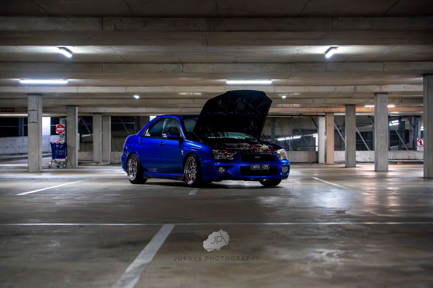 Dark green sports car parked in concrete parking structure under fluorescent lighting.