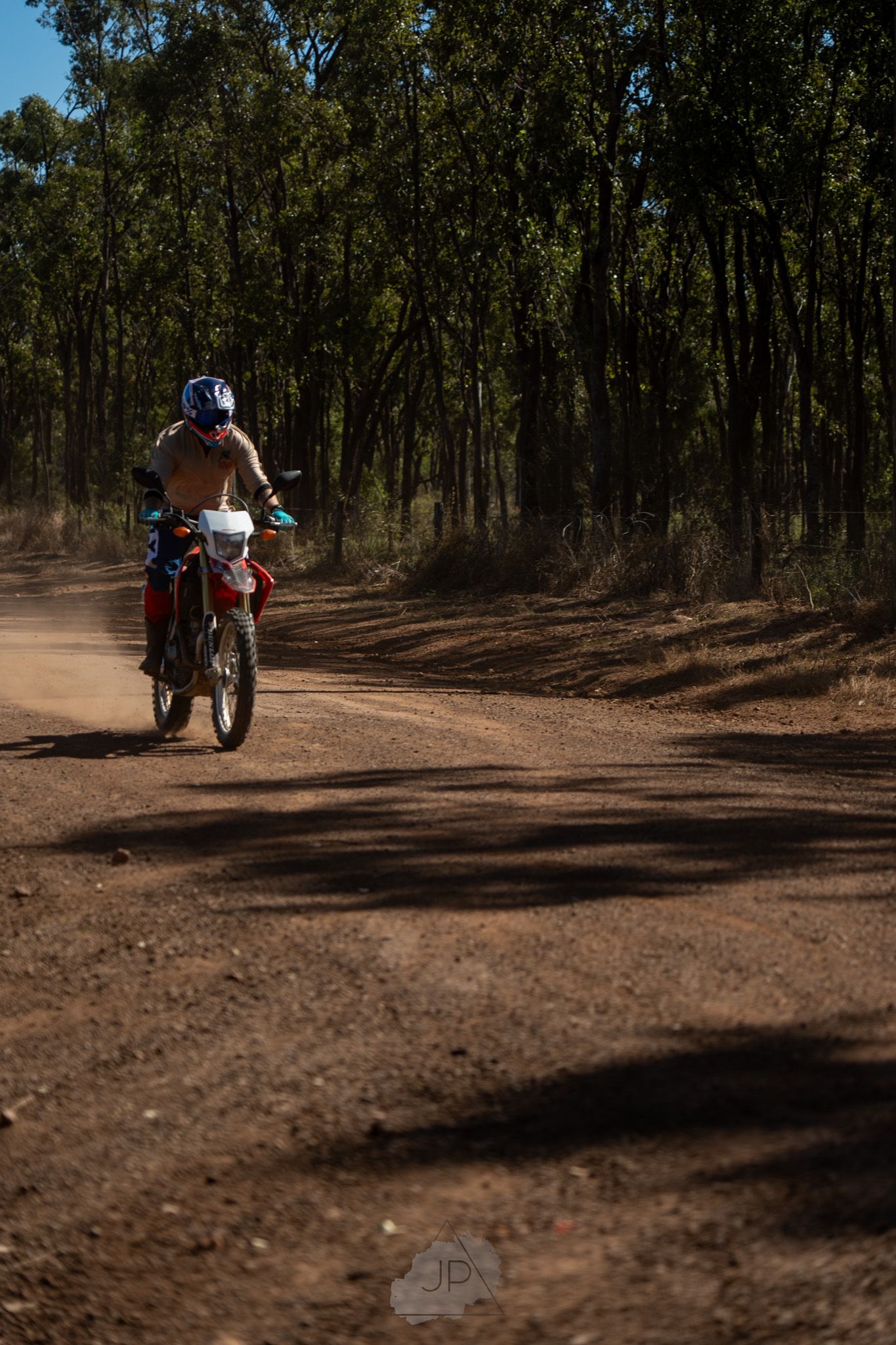 Series of dirt bike riders navigating a winding forest trail on a sunny day.