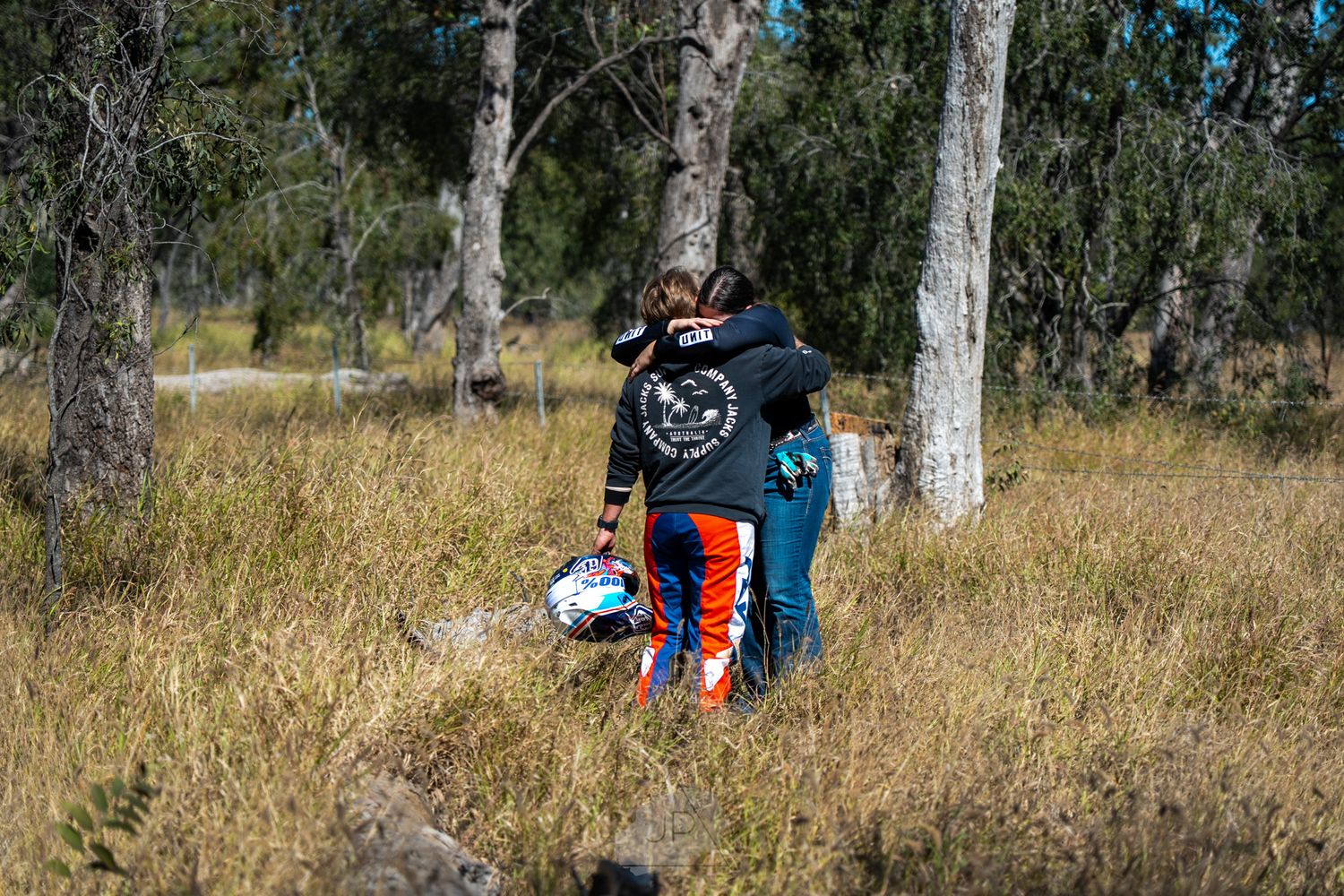 Someone wearing colorful outdoor gear explores a scenic wooded area with tall eucalyptus trees and dry grass.